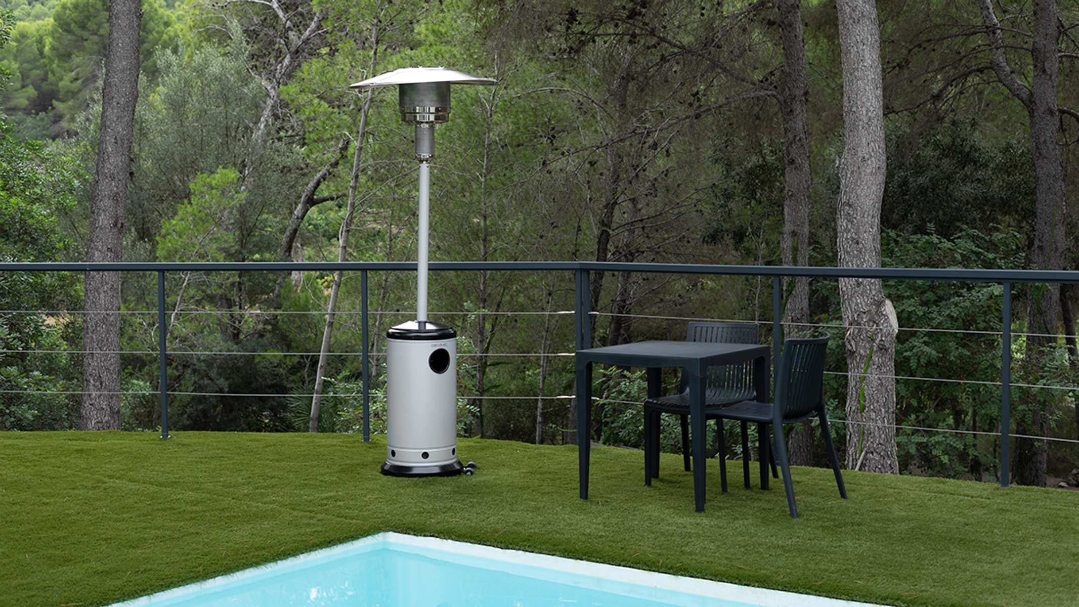 Escena de patio al aire libre con un calentador de patio plateado, mesa, sillas, piscina y árboles.