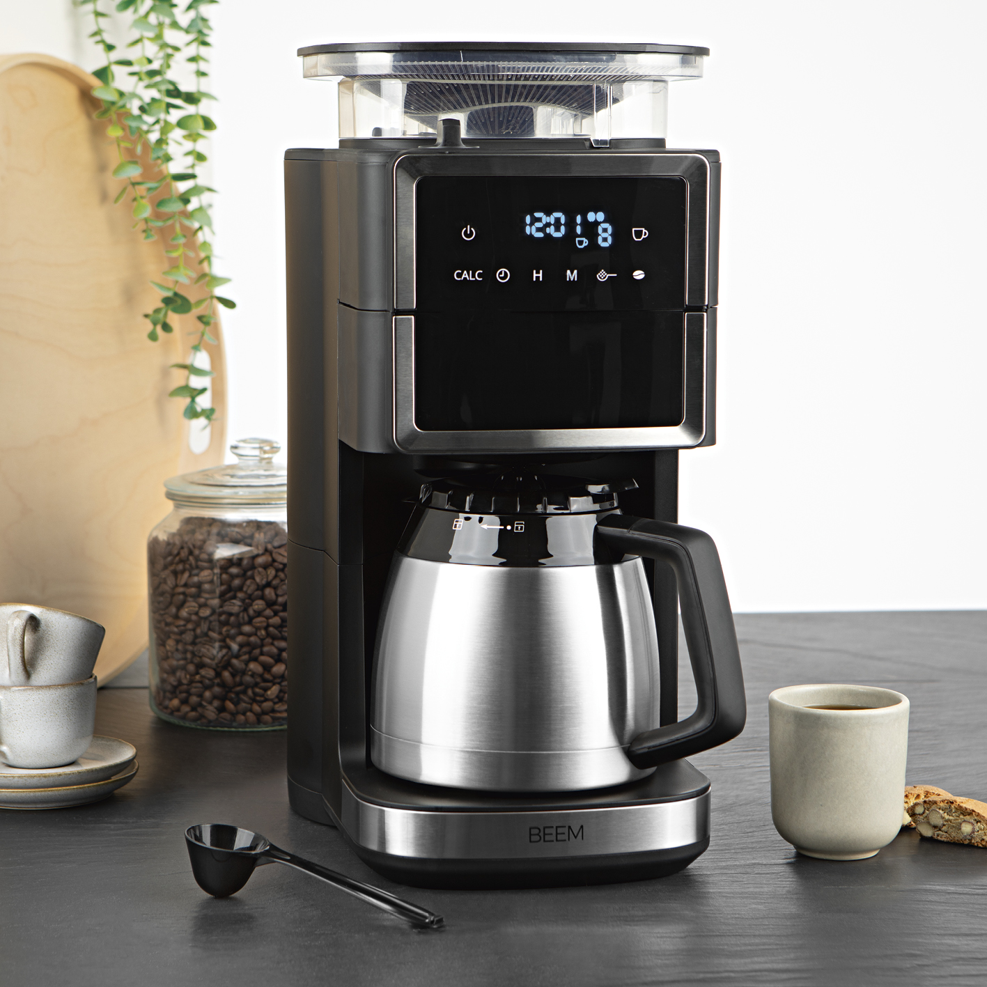 Ekspres do kawy ze stalowym dzbankiem, czarnym panelem sterowania i filiżanką kawy.