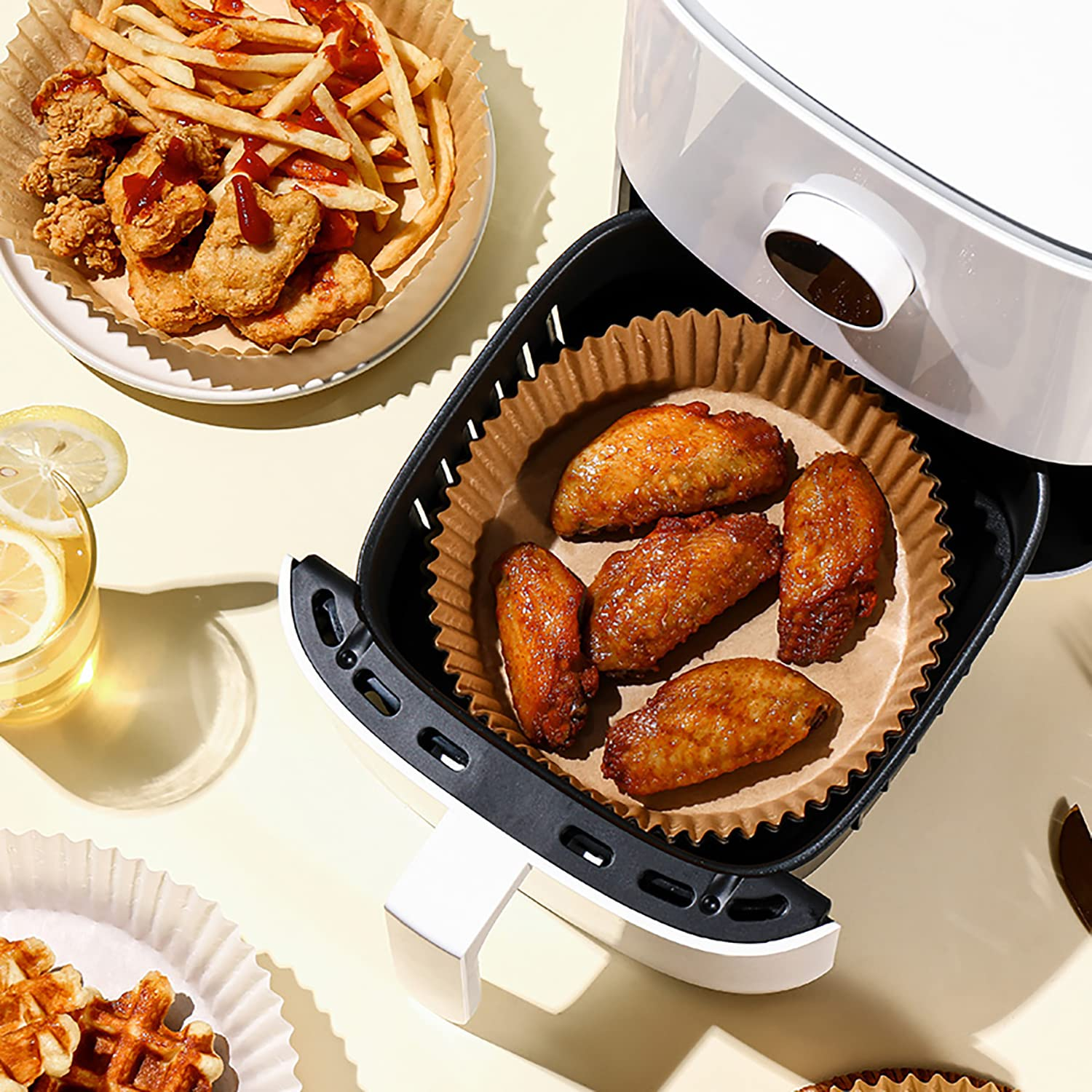 Heißluftfritteuse-Korb mit gekochten Hähnchenflügeln, Pommes und anderen Speisen.