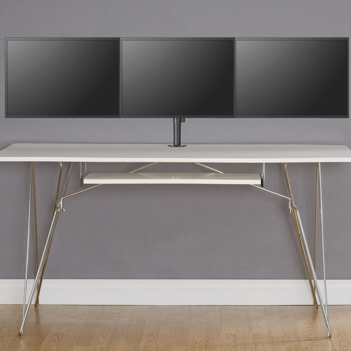 Drie zwarte monitoren op een witte bureau. Zilveren poten. Grijze muur op de achtergrond.
