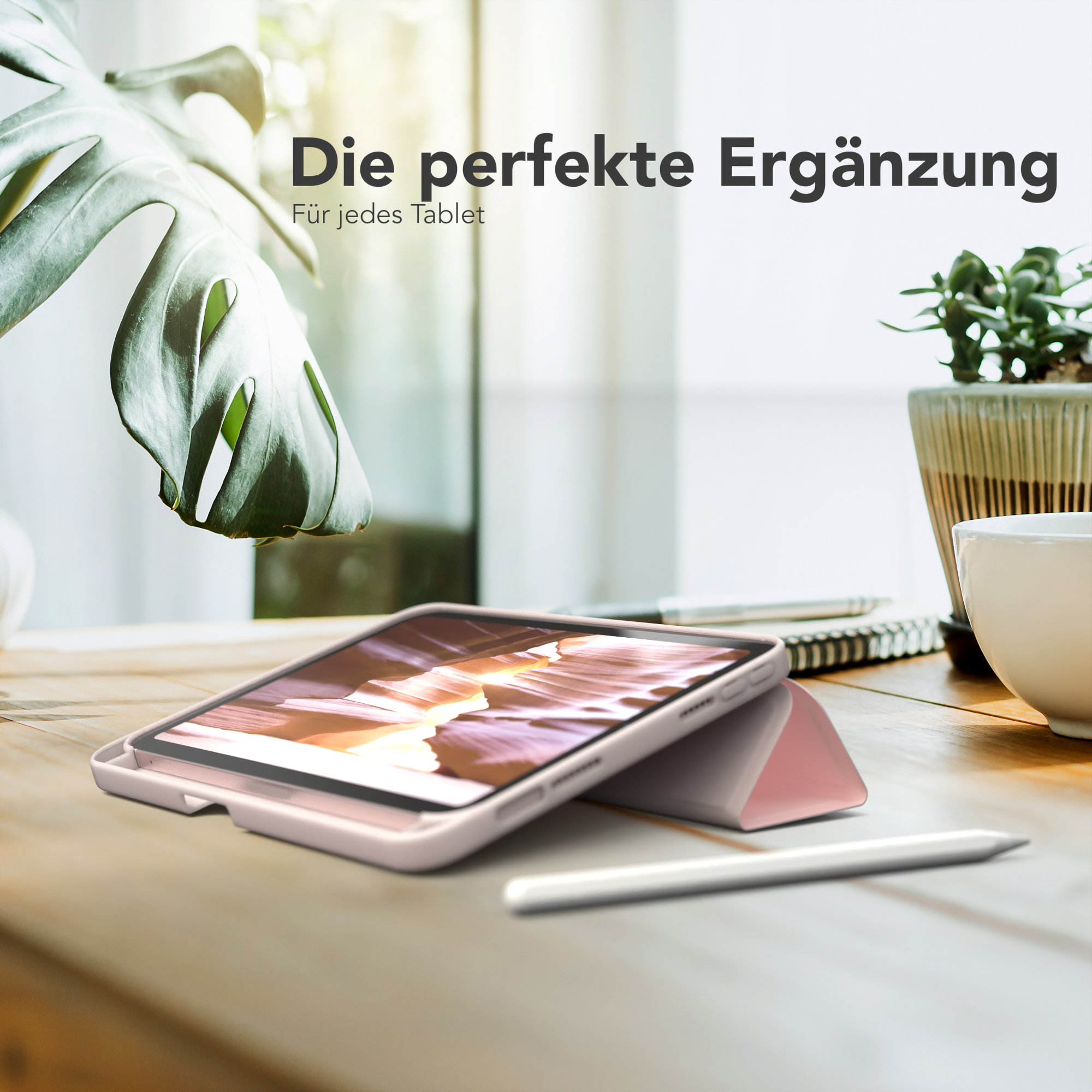 Tablet auf einem Holztisch, in einem rosa Gehäuse. Ein Stift liegt auf dem Tisch. Eine Pflanze im Hintergrund.