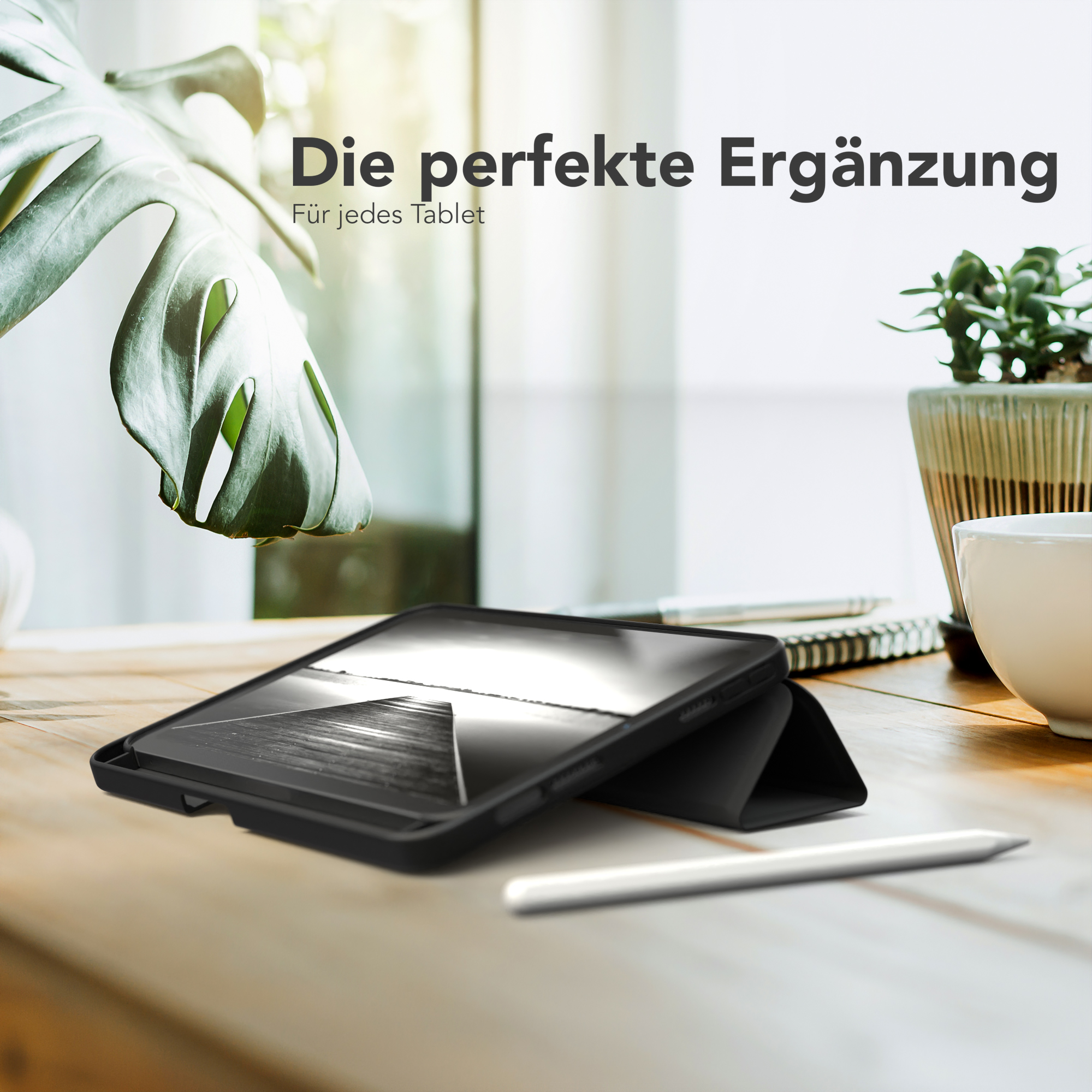 Tablet in einer schwarzen Hülle auf einem Holztisch, mit einem weißen Stift und Pflanze.