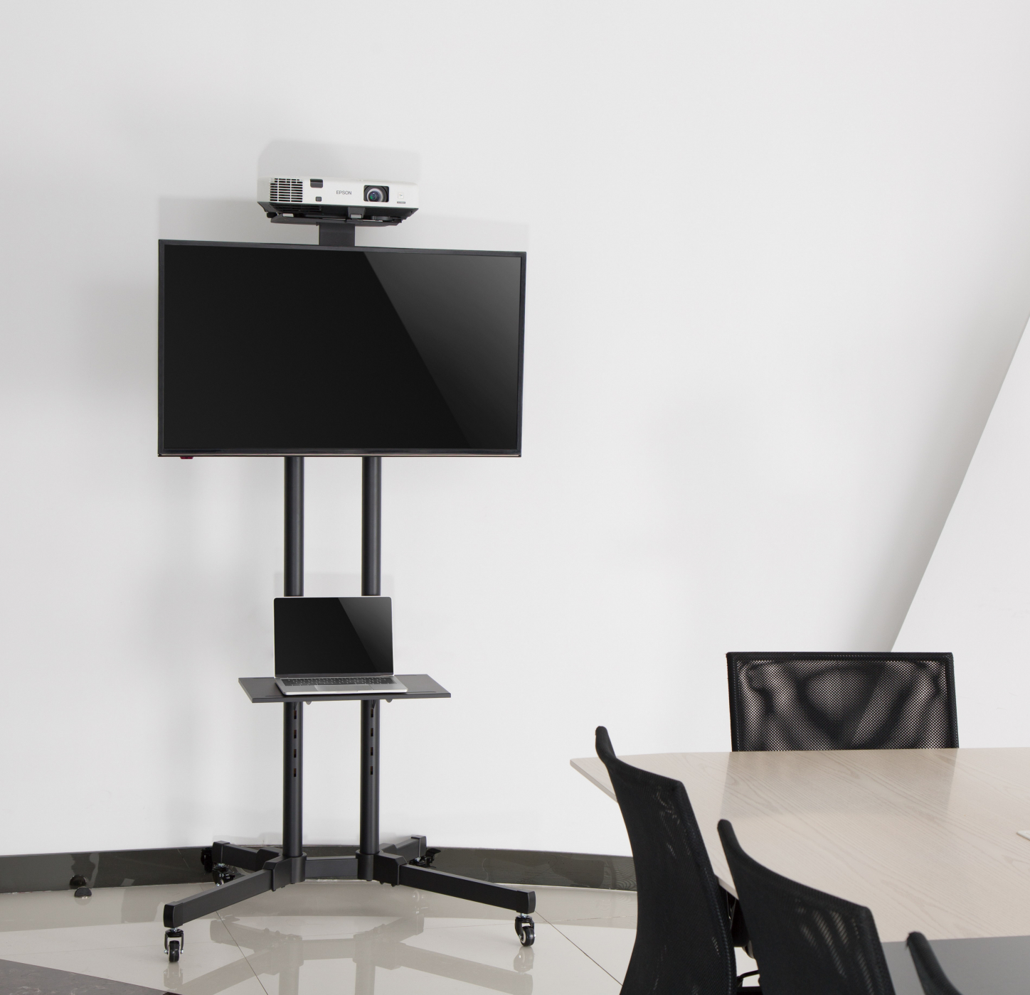 Conferentieruimte met tv, projector en laptop op een rolstandaard, bij een tafel en stoelen.