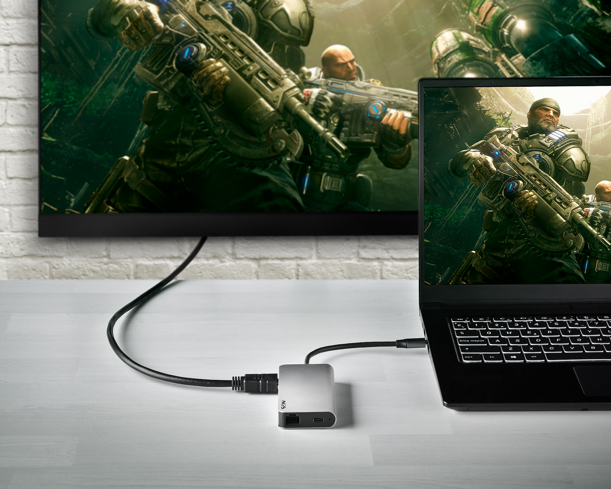 Laptop mit Fernseher verbunden, zeigt eine Videospielszen. Ein silberner Adapter wird verwendet.