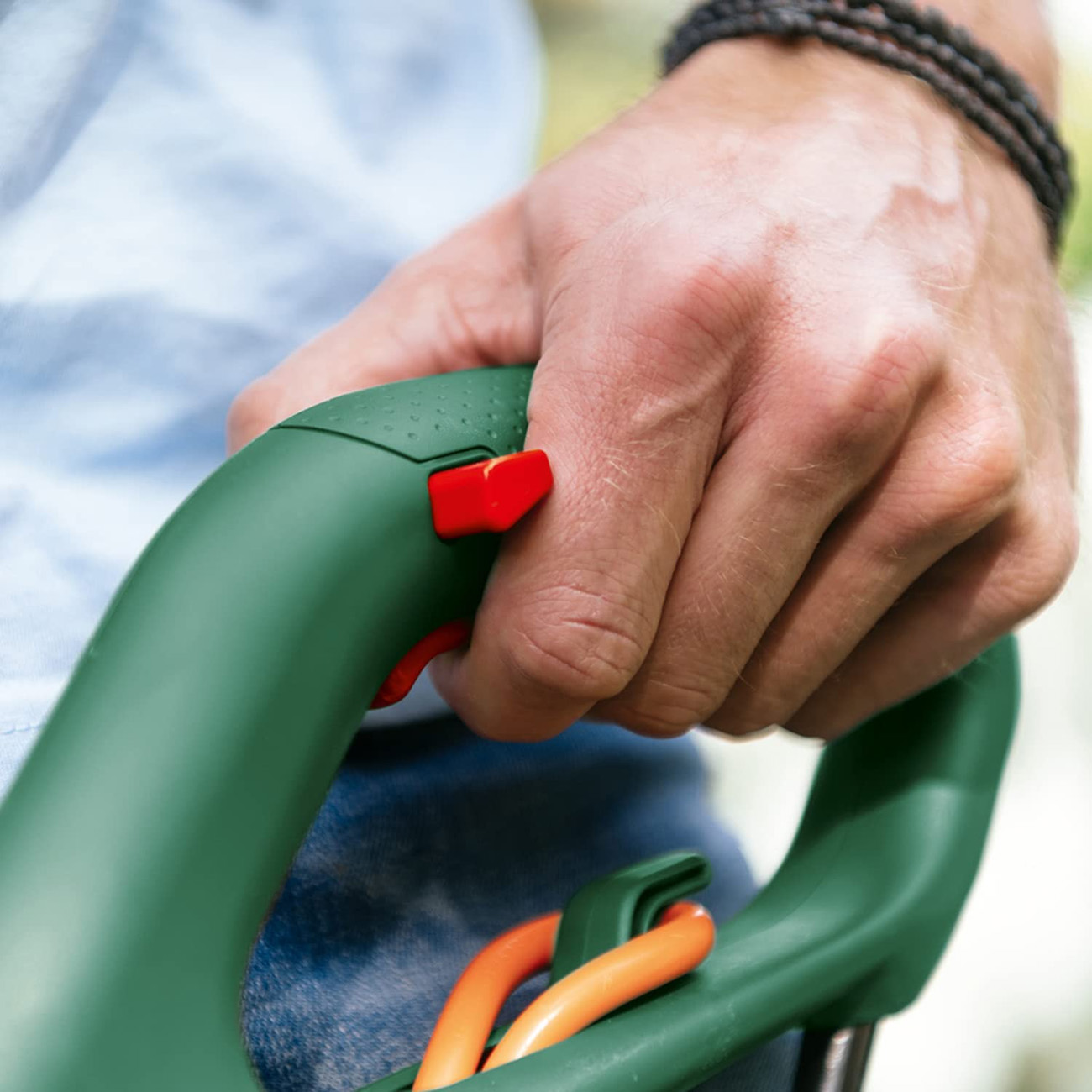 Een hand die een groen en oranje tuingereedschap vasthoudt.
