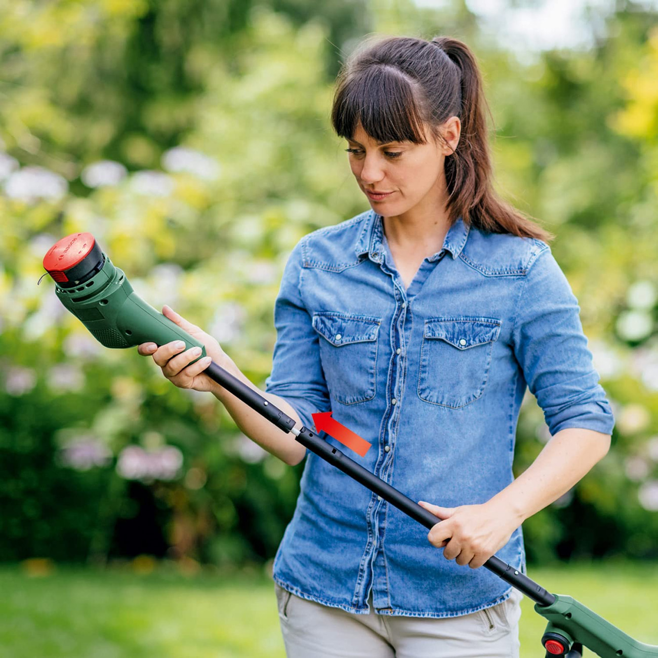 Une femme assemble un outil de jardinage vert et noir dans un jardin.
