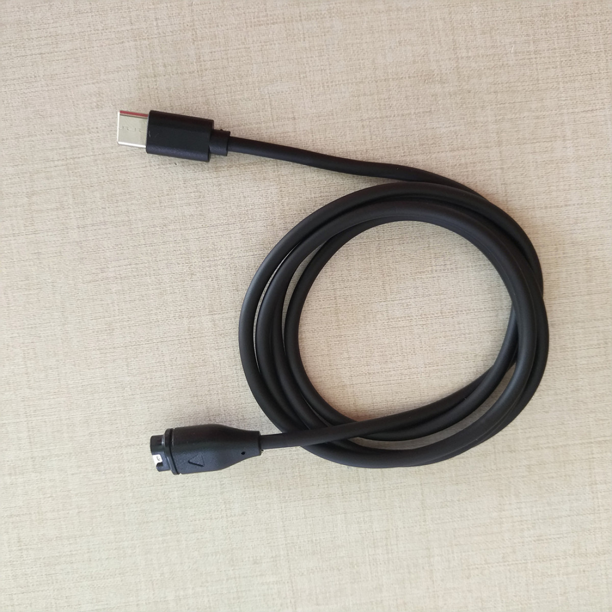 Zwarte USB-C-kabel met connectoren aan beide uiteinden, opgerold op een licht houten oppervlak.