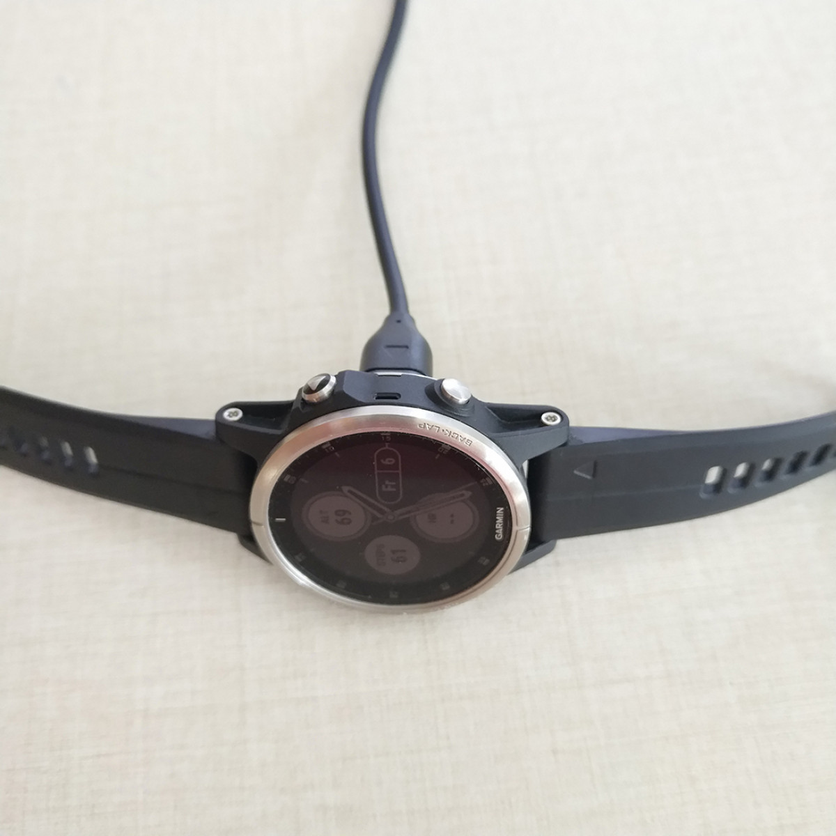 Smartwatch opladen op een licht oppervlak, zwarte band en wijzerplaat zichtbaar.