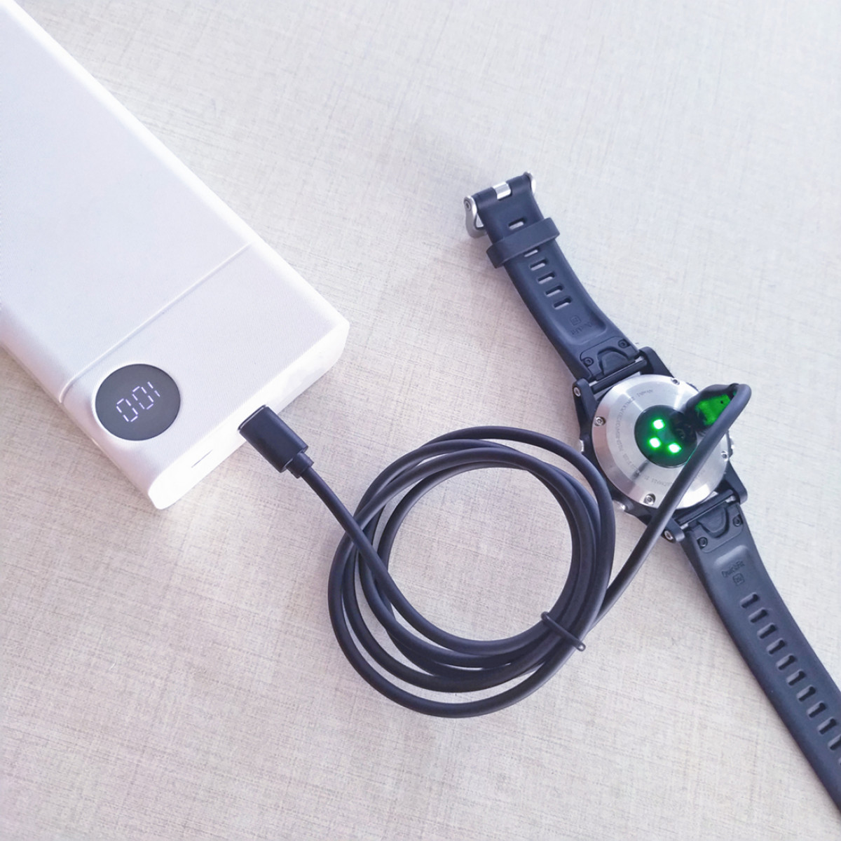 Een smartwatch aangesloten op een witte powerbank met een oplaadkabel op een licht oppervlak.