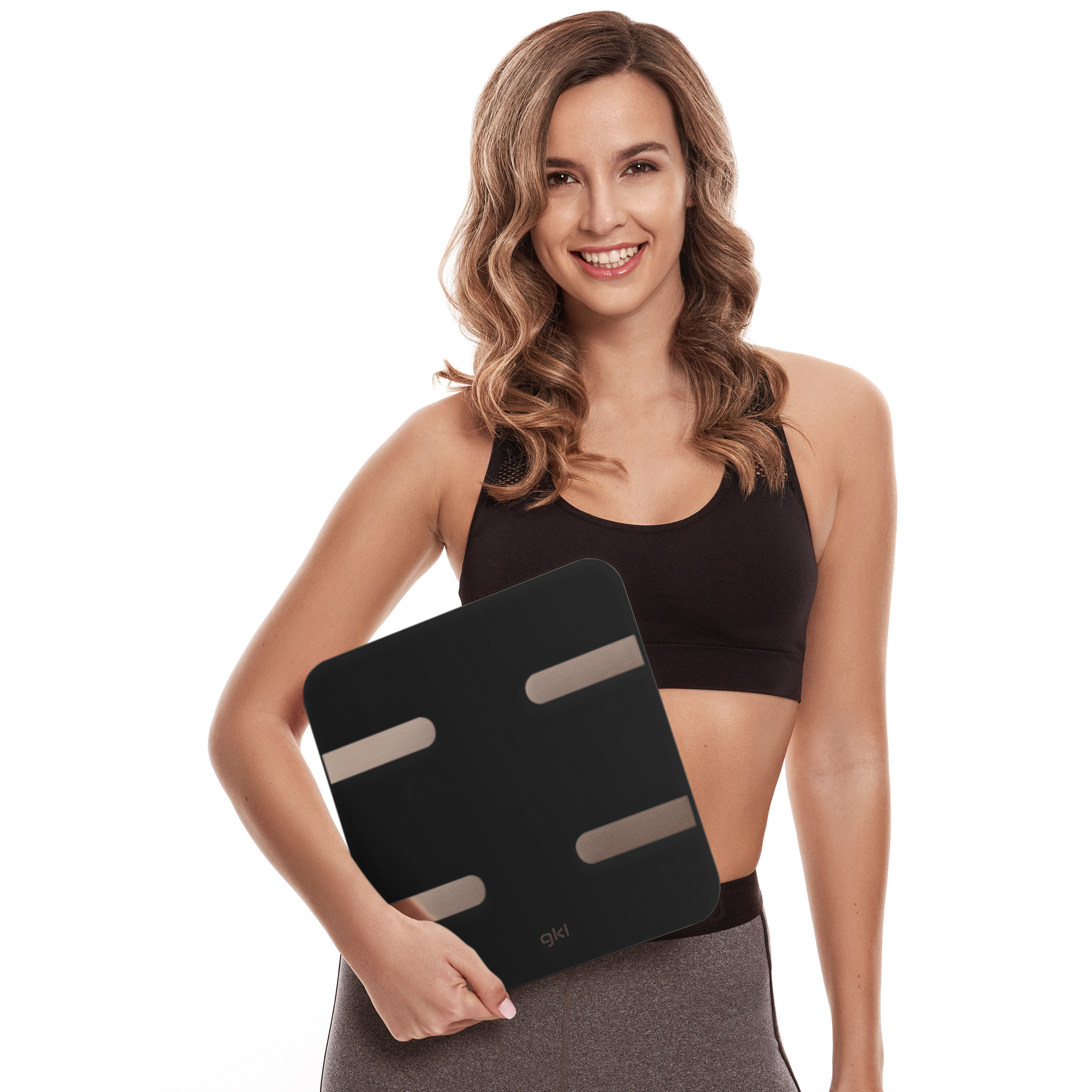 Mujer sosteniendo una báscula corporal negra, sonriendo. Viste top negro y leggings grises.