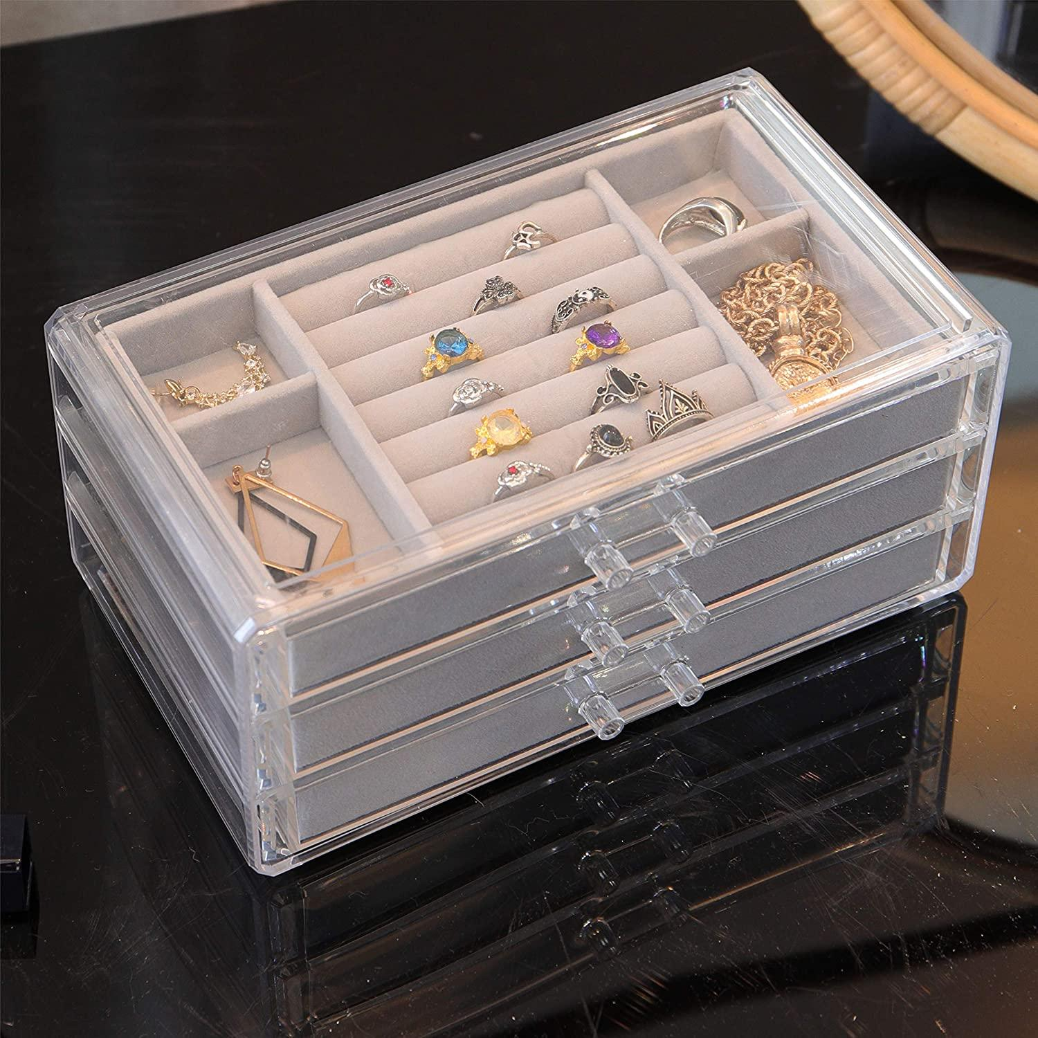 Ein klarer Schmuckorganizer mit Schubladen und Fächern, gefüllt mit Ringen und Ohrringen.