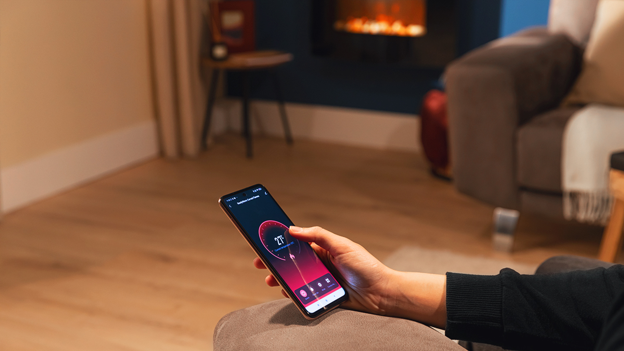 Una mano sostiene un teléfono que muestra una interfaz de hogar inteligente en una sala de estar.