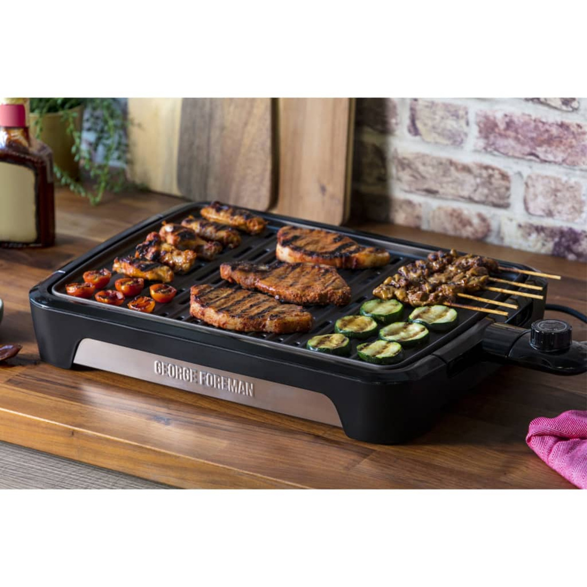 Griglia George Foreman con cibo grigliato. Include bistecca, verdure e spiedini su una superficie di legno.