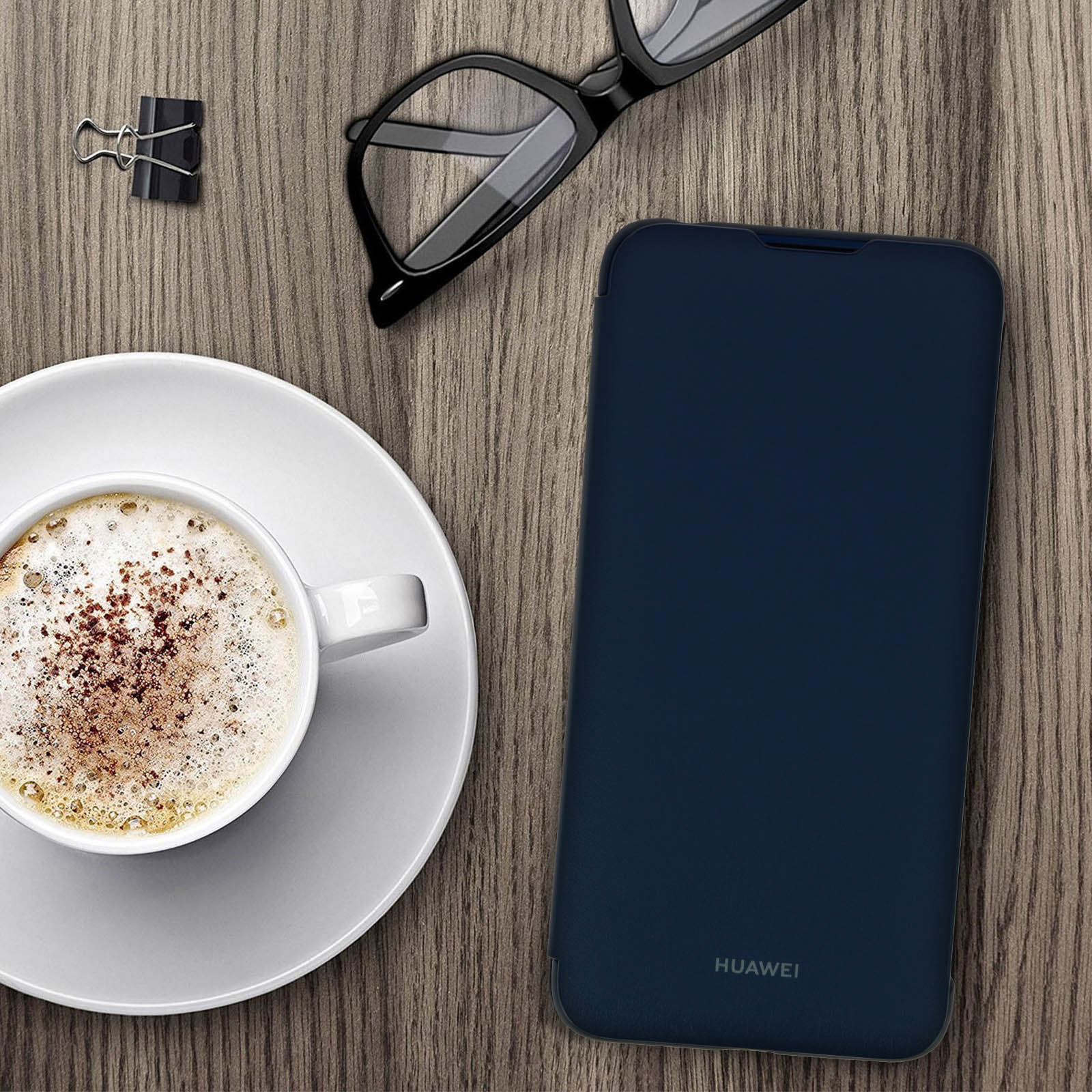 Una custodia blu navy su un tavolo di legno. Accanto, caffè, occhiali e graffetta.