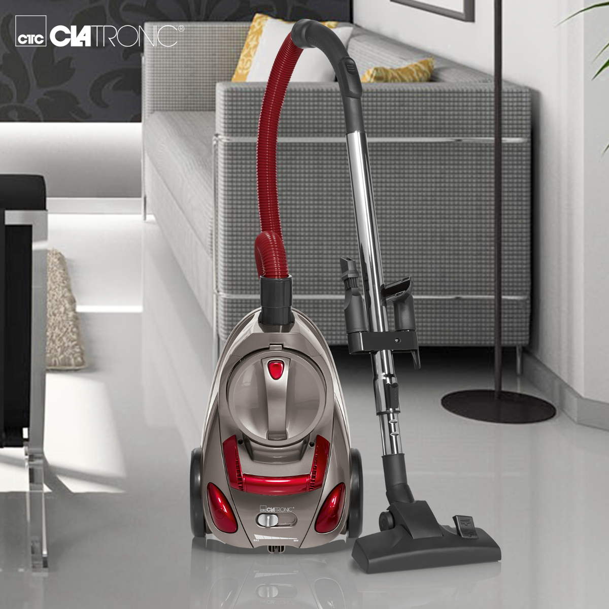 Srebrno-czerwony odkurzacz na szarej i białej podłodze. Ma czerwony wąż i czarną dyszę.