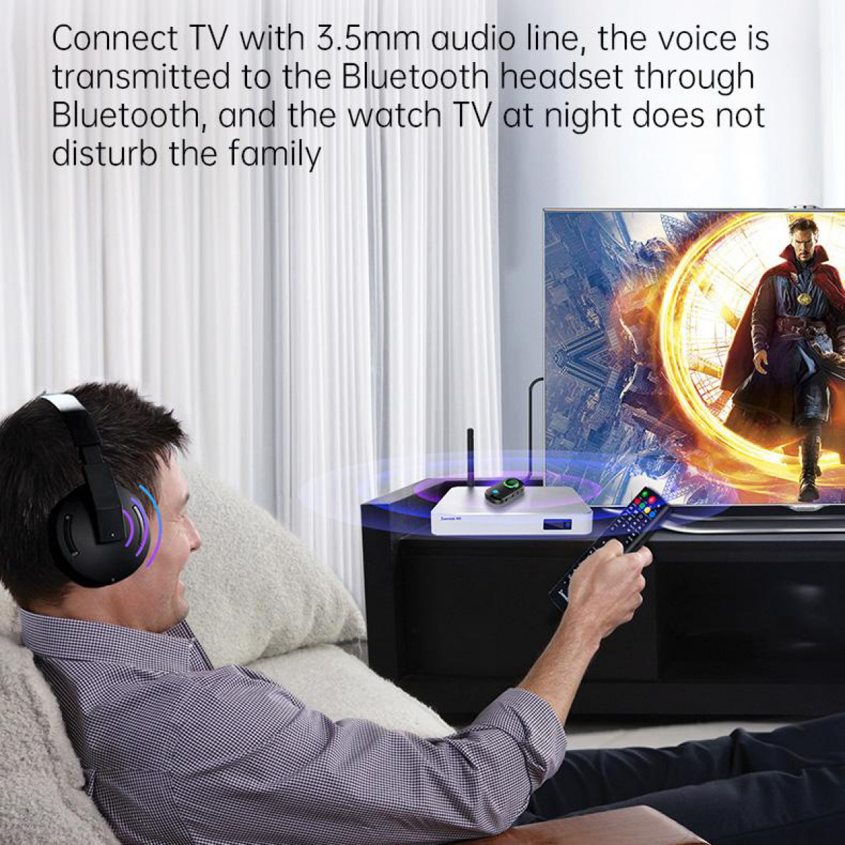 Mężczyzna w słuchawkach ogląda TV. TV pokazuje mężczyznę w czerwonym płaszczu. Urządzenie na stole.