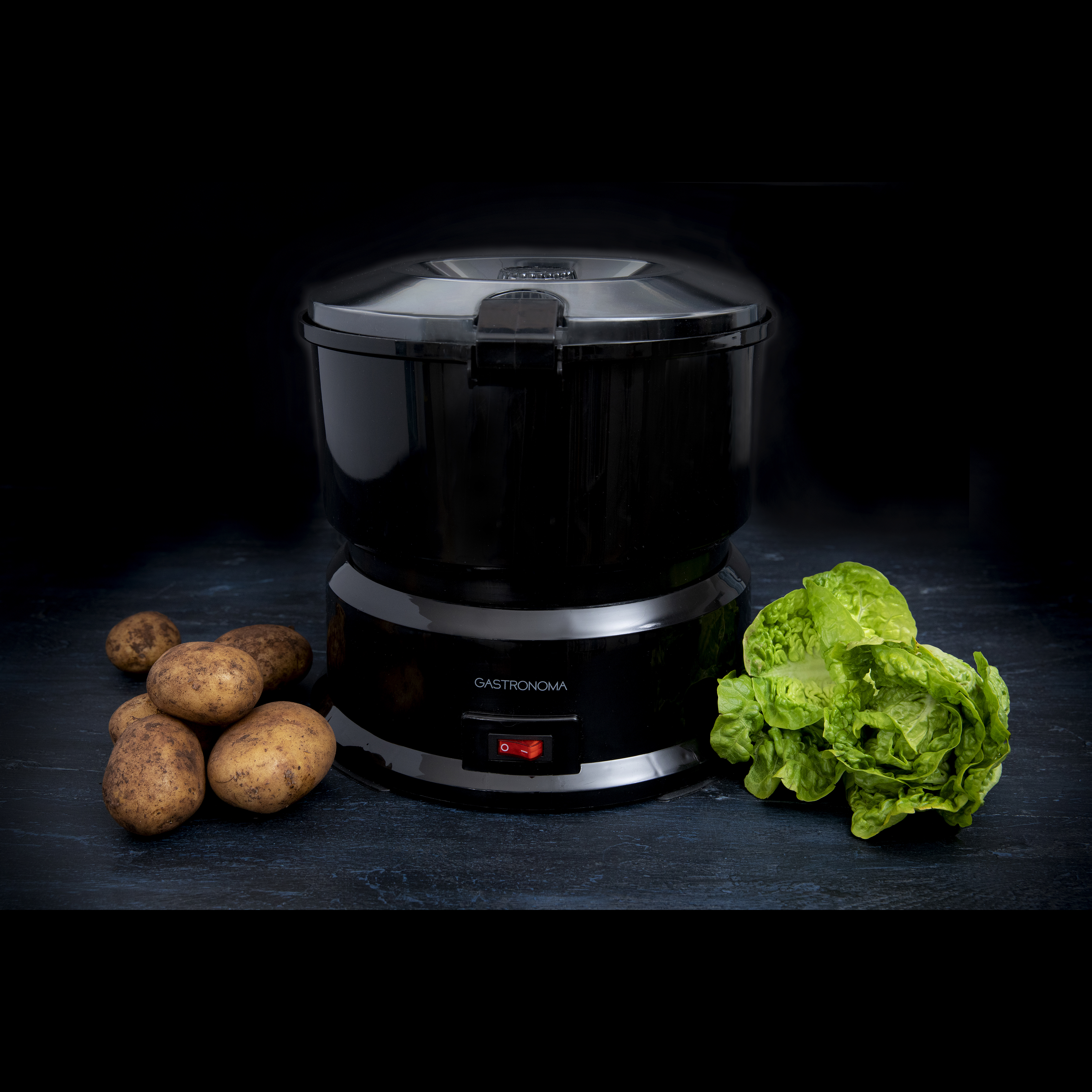 Czarne urządzenie kuchenne z ziemniakami i sałatą, na ciemnej powierzchni. Czarne tło.