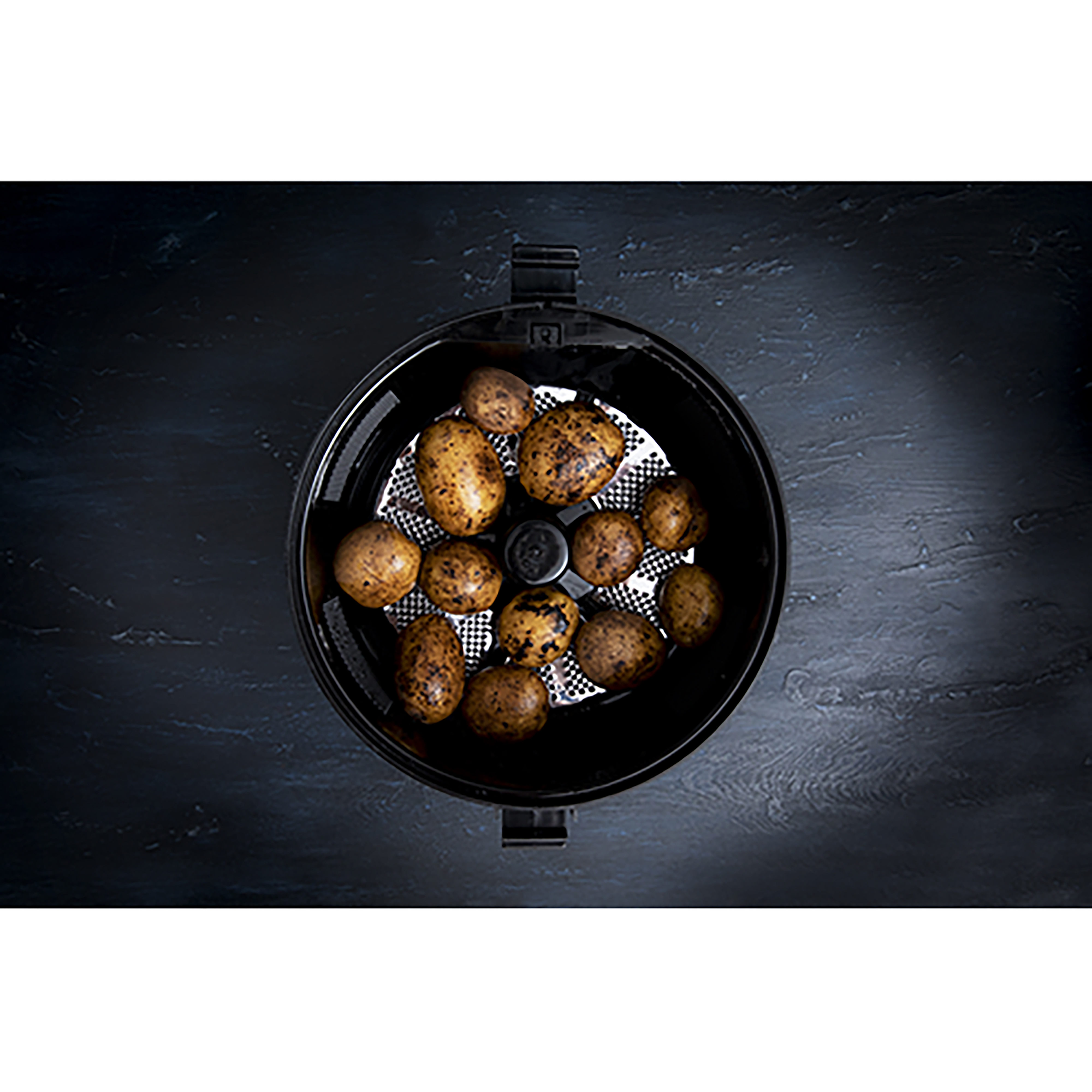 Czarny kosz do frytkownicy powietrznej z ziemniakami w środku, na ciemnoniebieskiej, teksturowanej powierzchni.