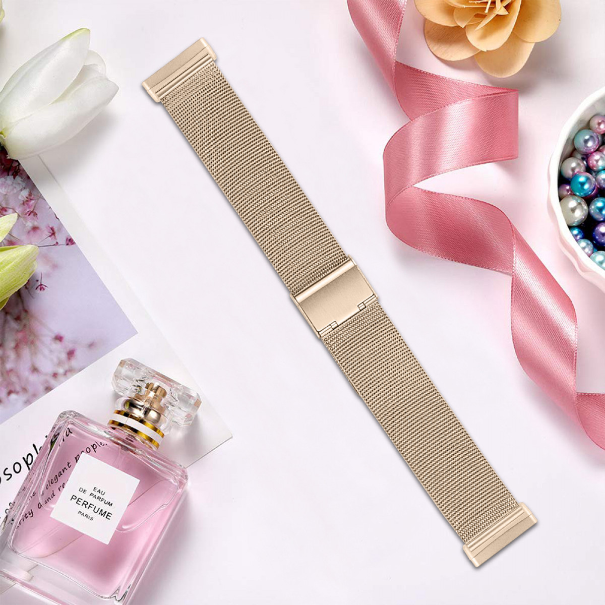 Goldenes Uhrenarmband mit Parfümflasche, rosa Schleife und einer Schale mit Perlen.