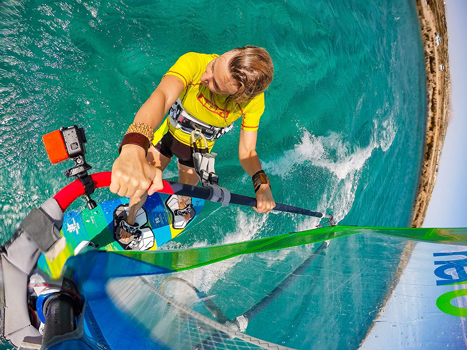 Osoba uprawiająca windsurfing na turkusowej wodzie, ujęcie z niskiego kąta.