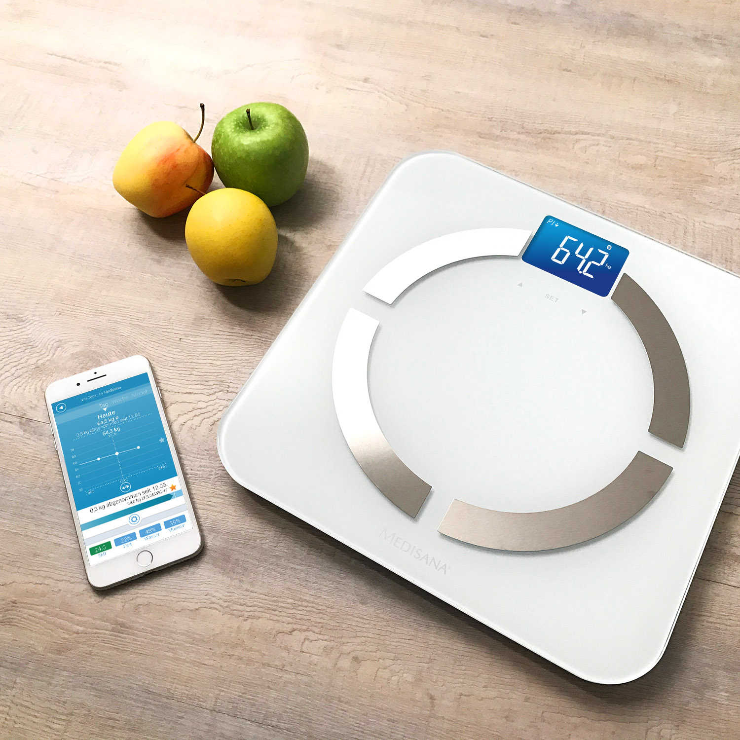 Waga cyfrowa z wyświetlaczem 64,2, smartfonem i trzema owocami na drewnianej powierzchni.