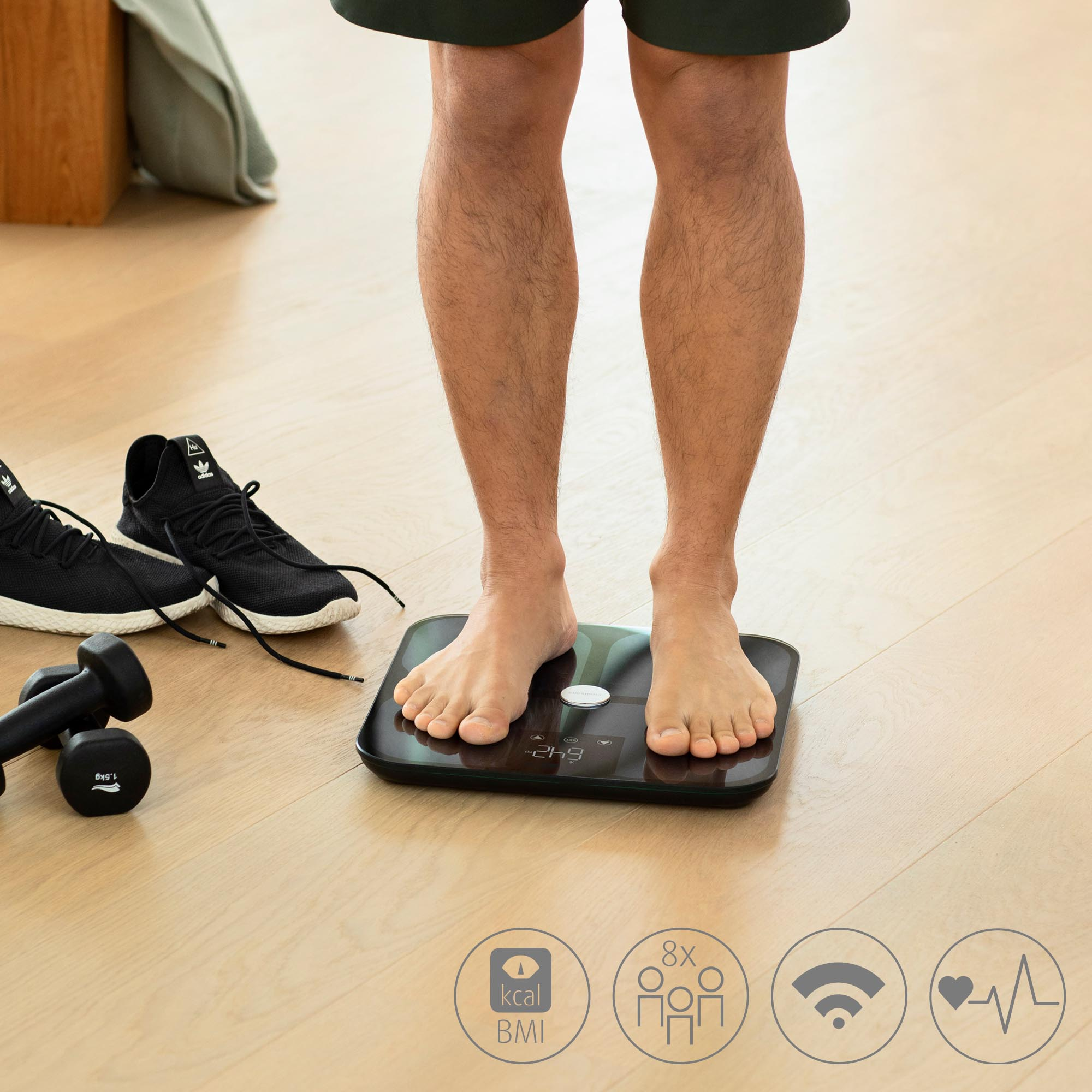 Uomo in piedi su una bilancia digitale. Scarpe e manubri neri sul pavimento.