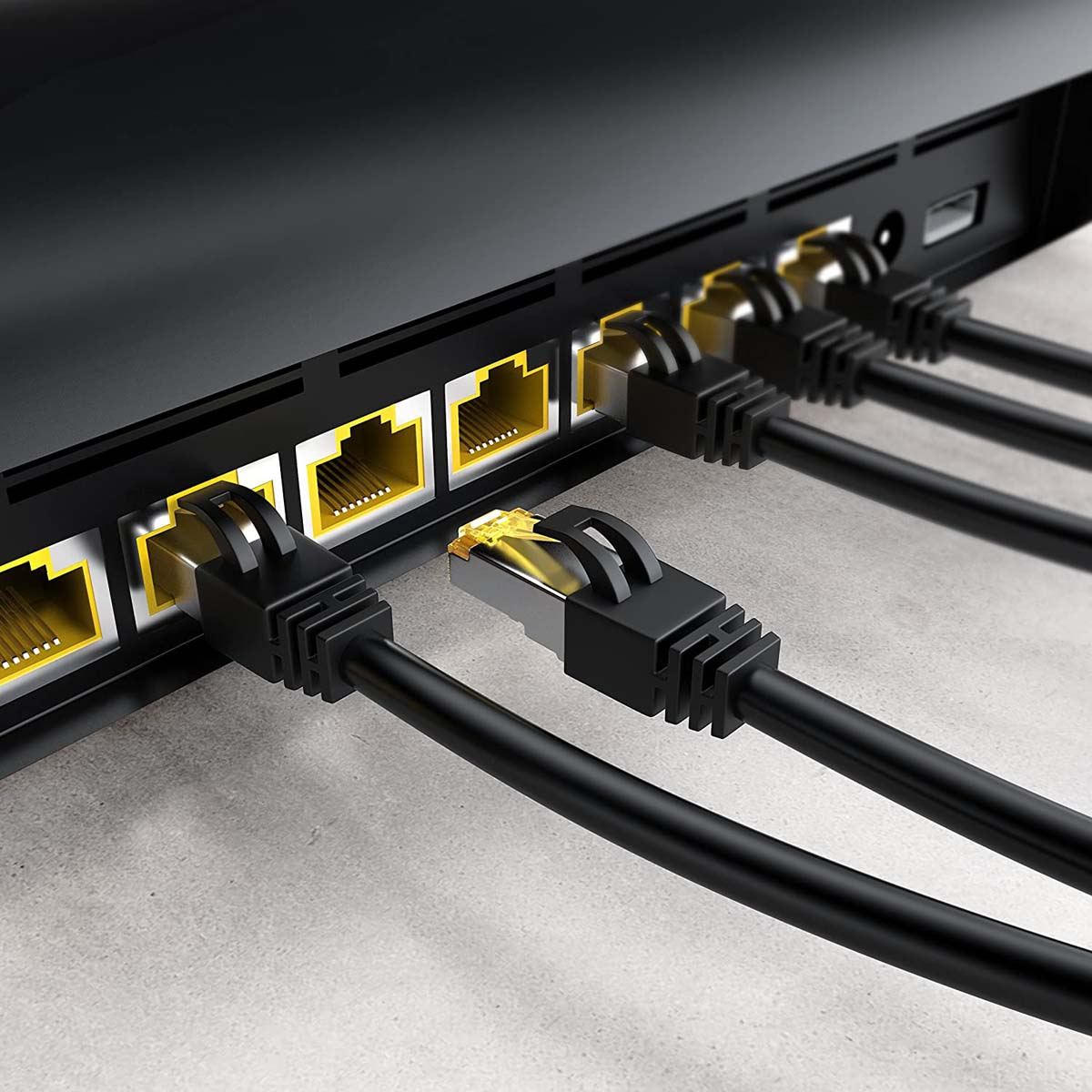 Czarne kable Ethernet podłączone do czarnego przełącznika sieciowego z żółtymi portami. Zbliżenie na jasnoszarej powierzchni.