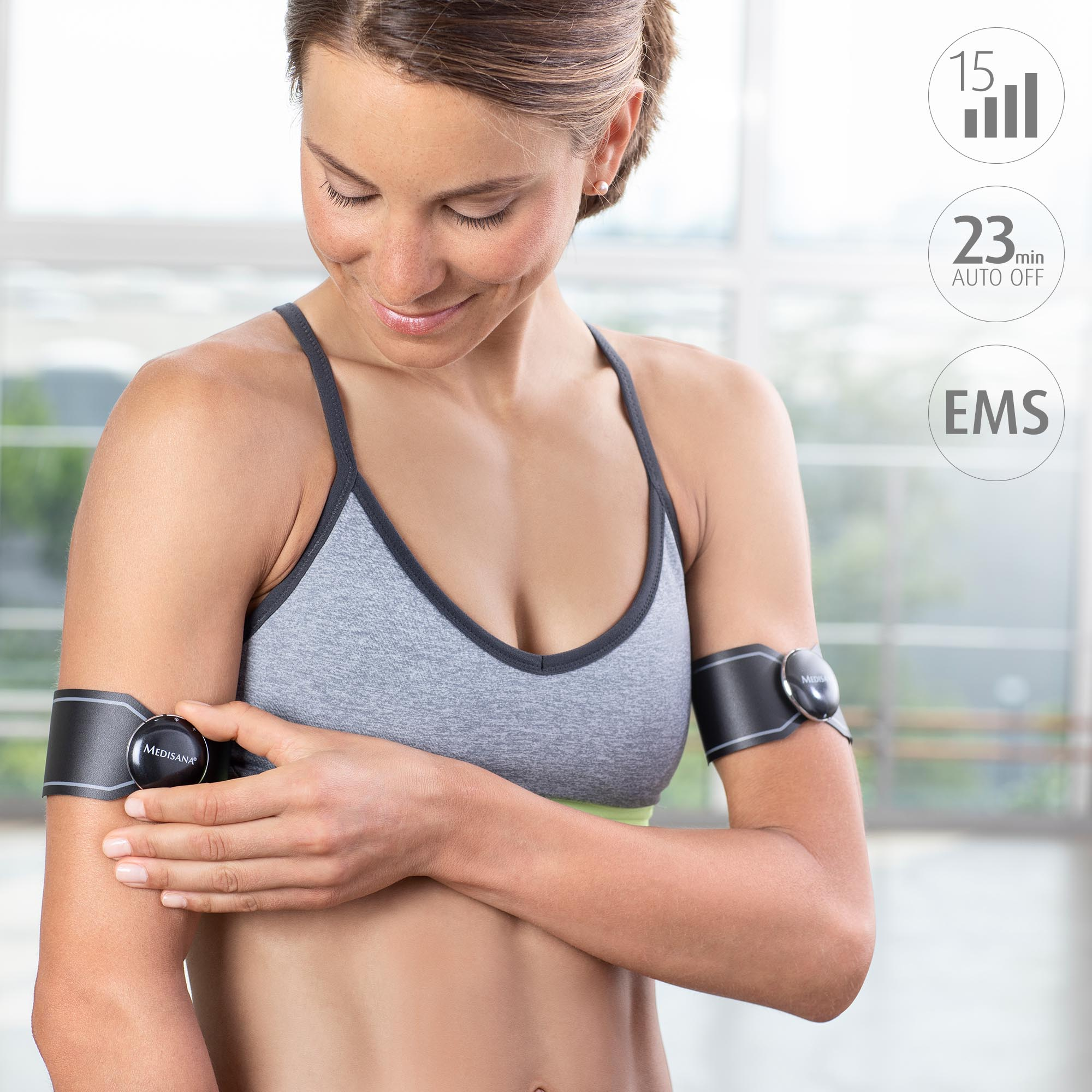 Mujer con sujetador deportivo gris y un estimulador muscular de brazo con iconos de temporizador y ajustes.