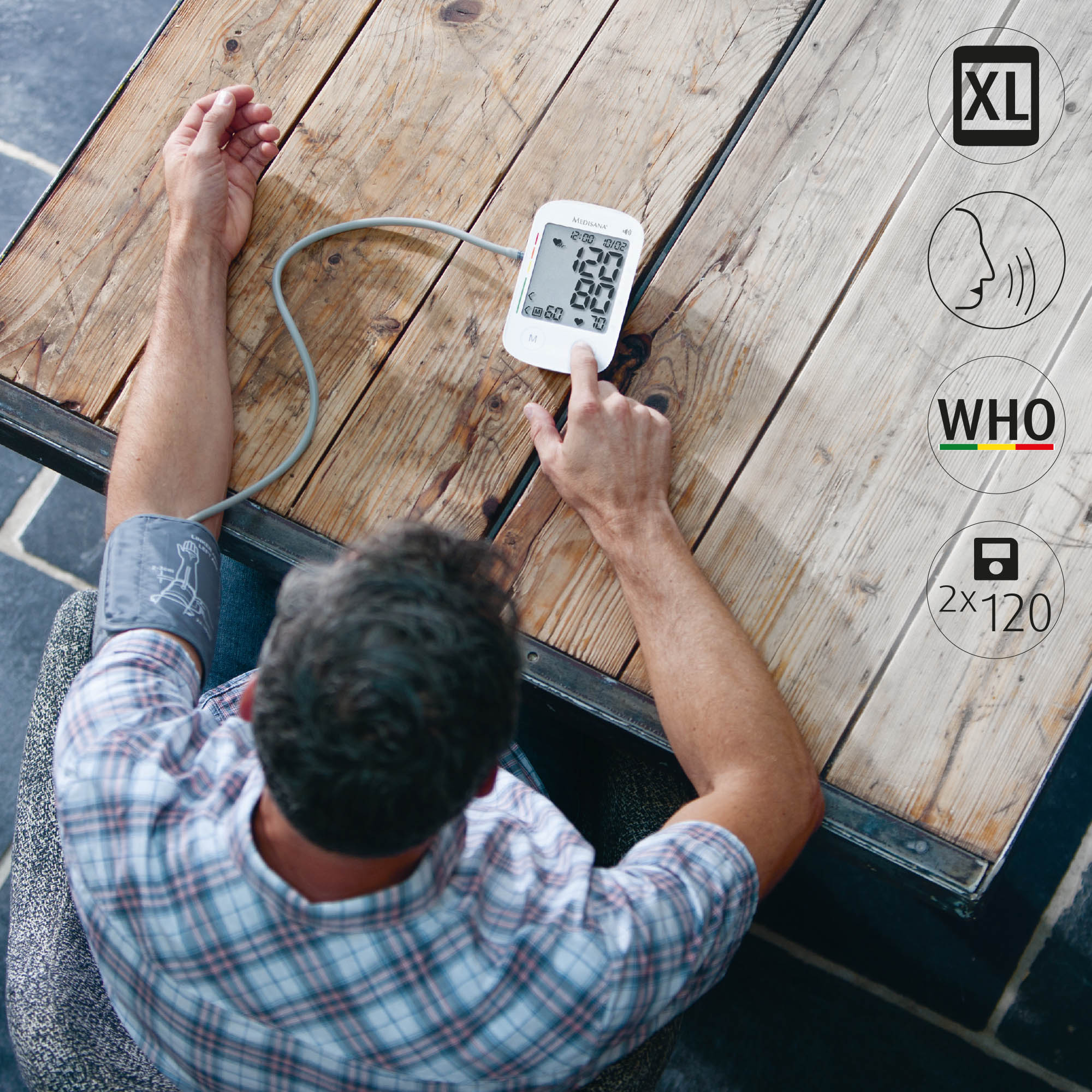 Osoba używająca białego monitora ciśnienia krwi na drewnianym stole z ikonami XL, głos, WHO i 2x120.
