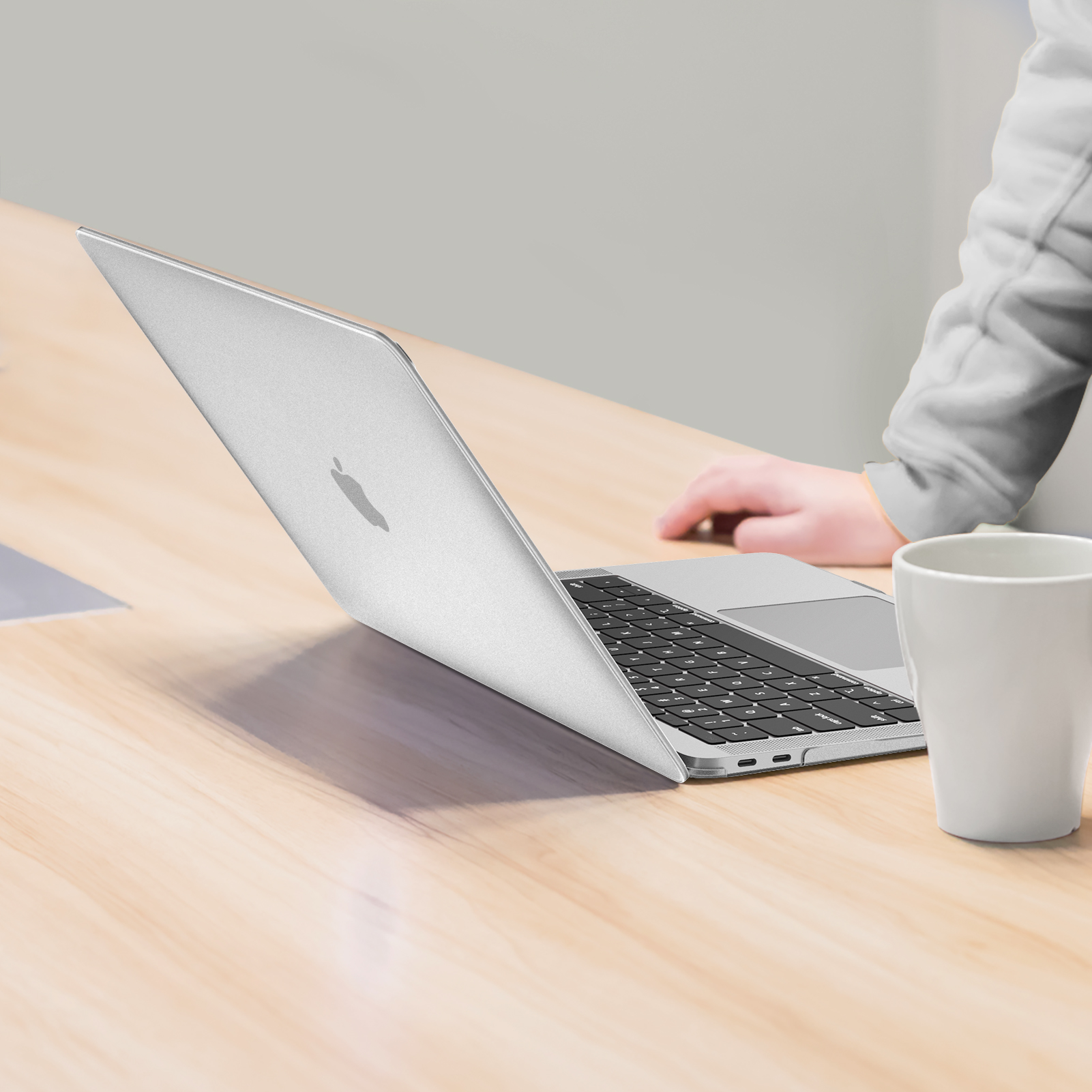 Silberner Laptop auf Holztisch. Eine weiße Tasse steht rechts. Hand auf dem Laptop.