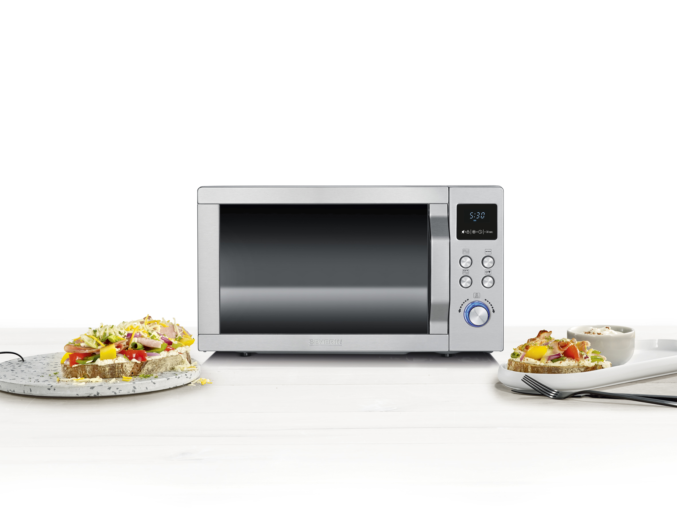 Srebrna kuchenka mikrofalowa z zamkniętymi drzwiami. Obok znajdują się dwa kawałki chleba z dodatkami.