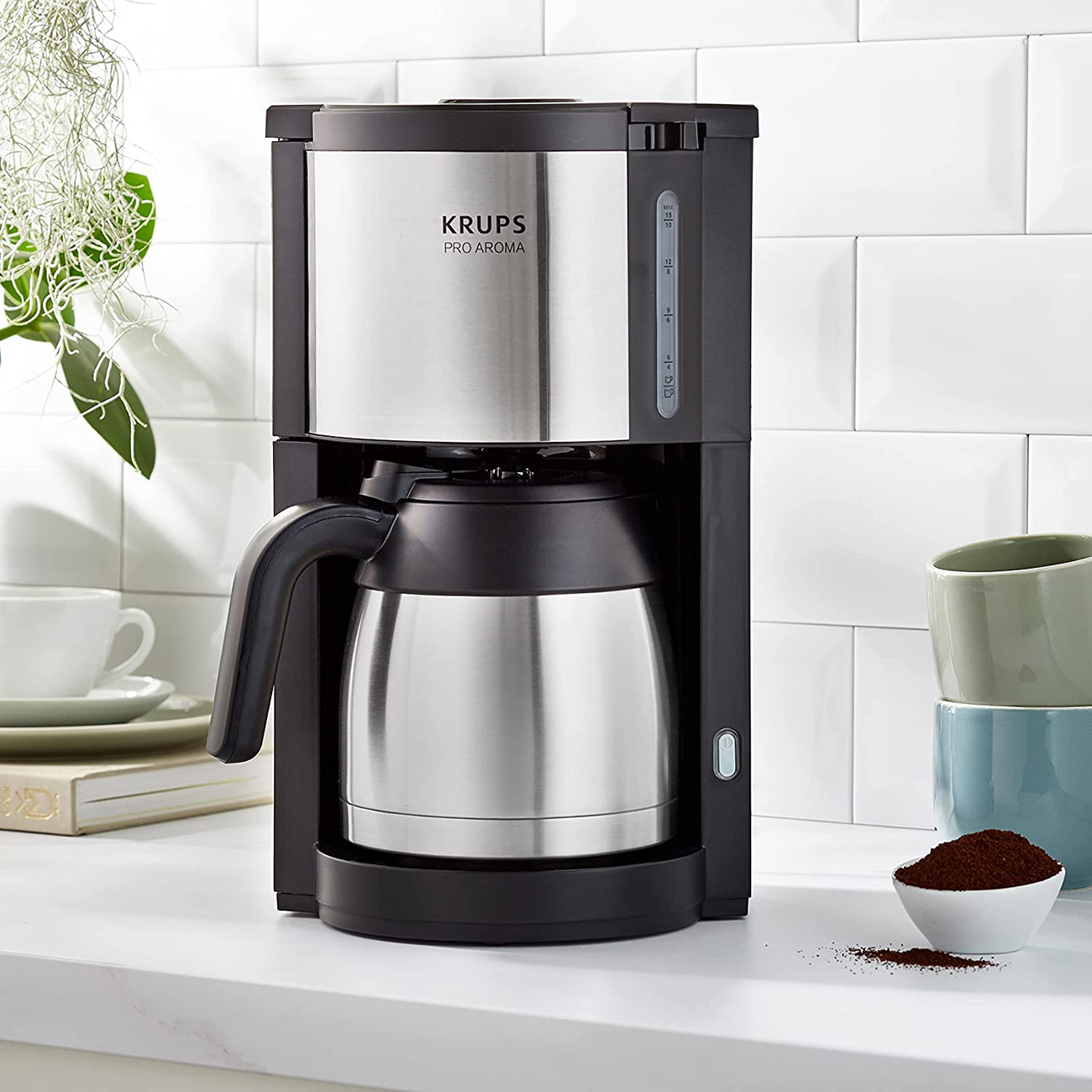 Kaffeemaschine mit schwarzem Gehäuse und silberner Thermokanne. Eine kleine Schale mit Kaffeepulver daneben.