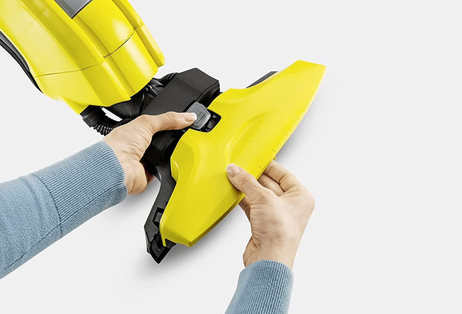 Manos acoplando un accesorio amarillo a un dispositivo de limpieza.