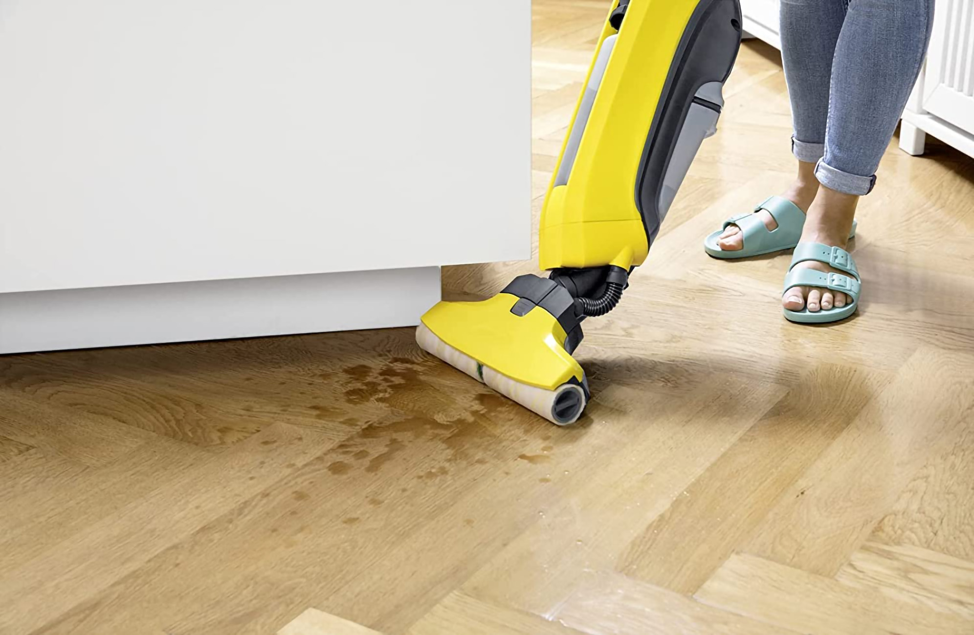Máquina de limpieza de pisos amarilla y negra en uso. Una persona está cerca con sandalias. Piso de madera.