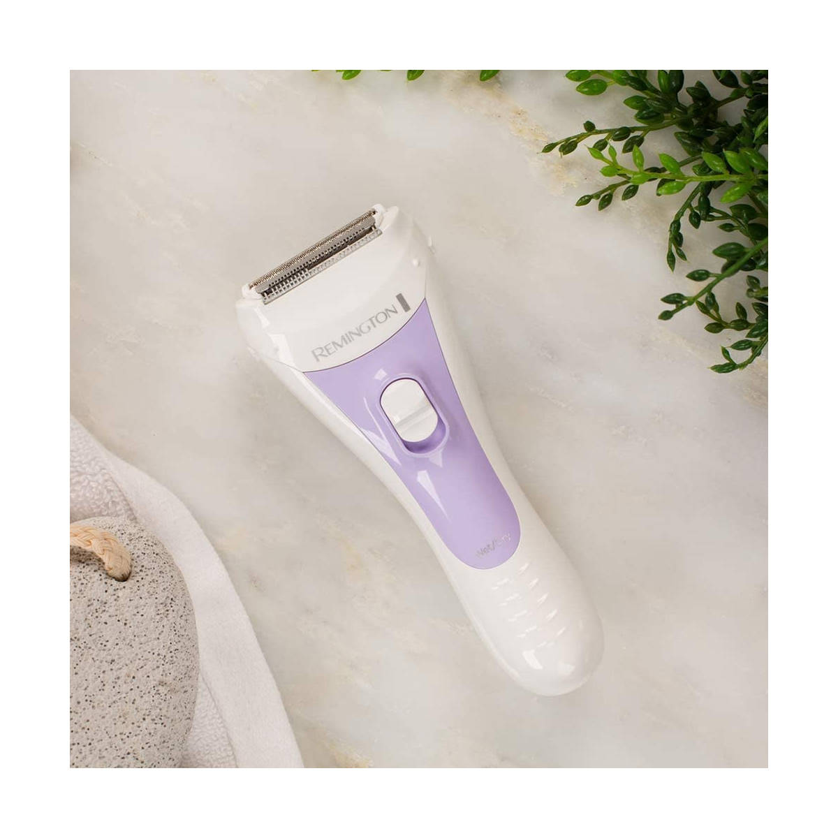 Biała i fioletowa golarka elektryczna Remington na białej powierzchni. Zielone liście w tle.