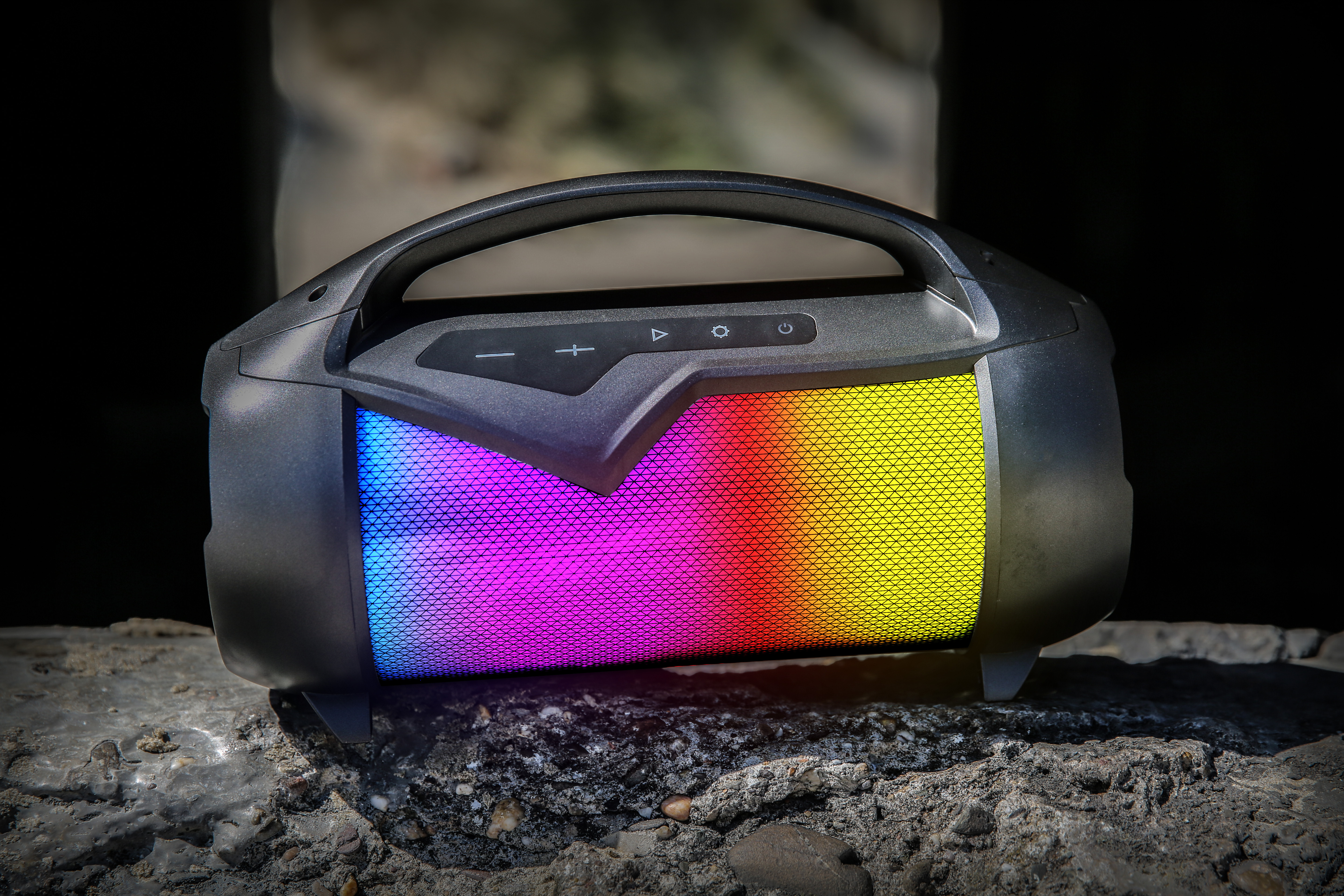Czarny głośnik z wielokolorowymi światłami, przyciskami na górze, na ciemnym tle.