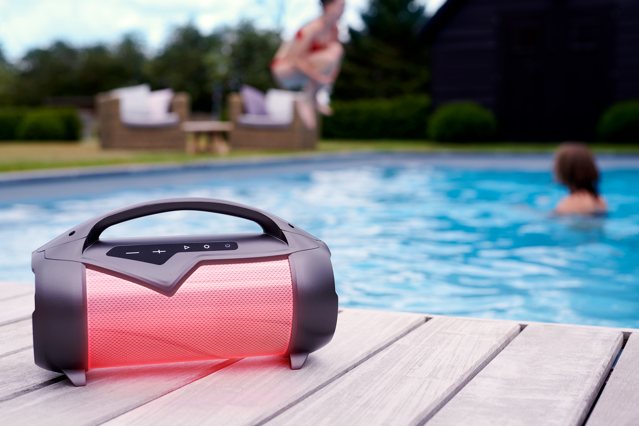 Głośnik na drewnianym tarasie obok basenu. Ludzie są w tle.
