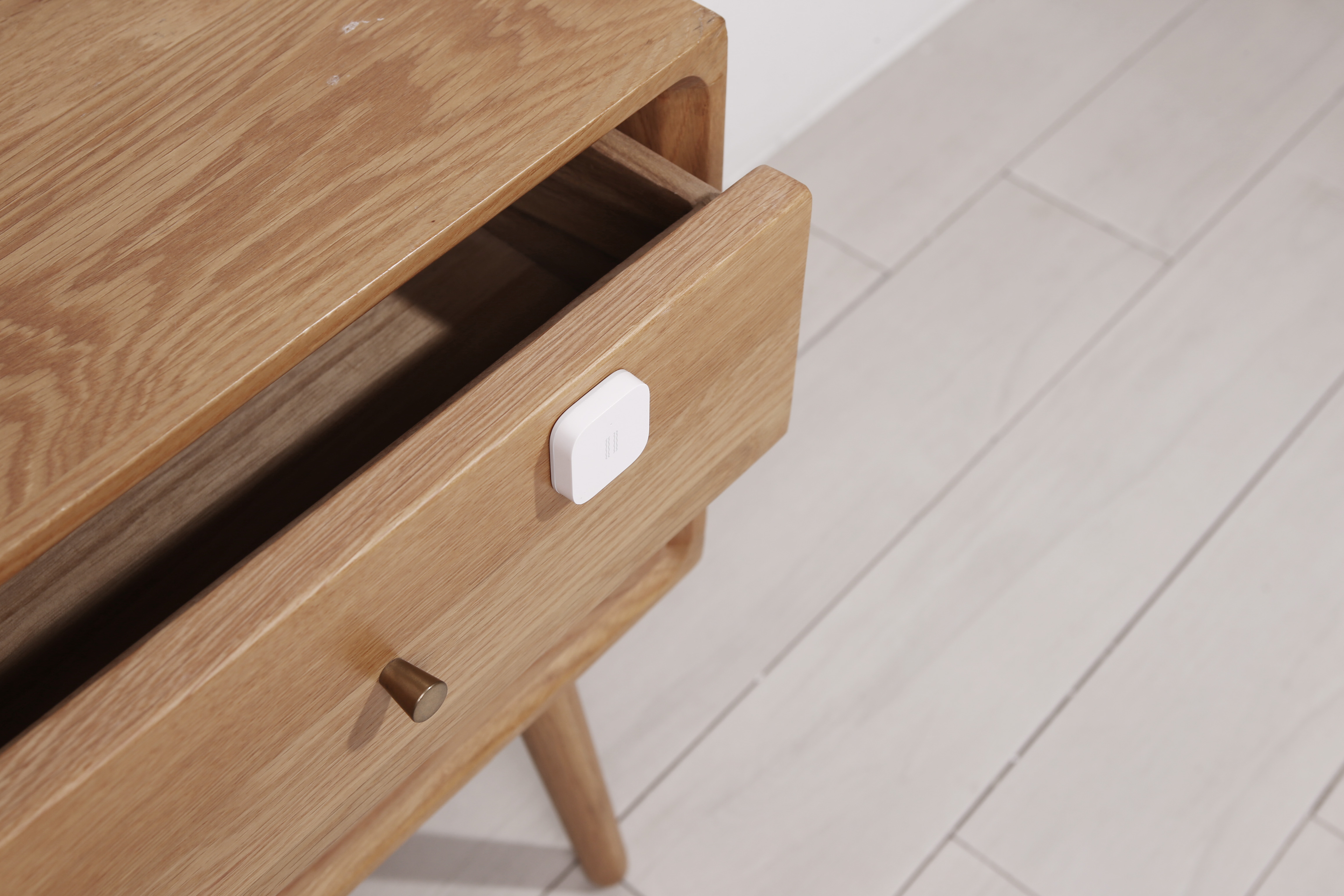 Ein weißer Smart-Home-Sensor auf einer offenen Holzschublade eines Schranks.