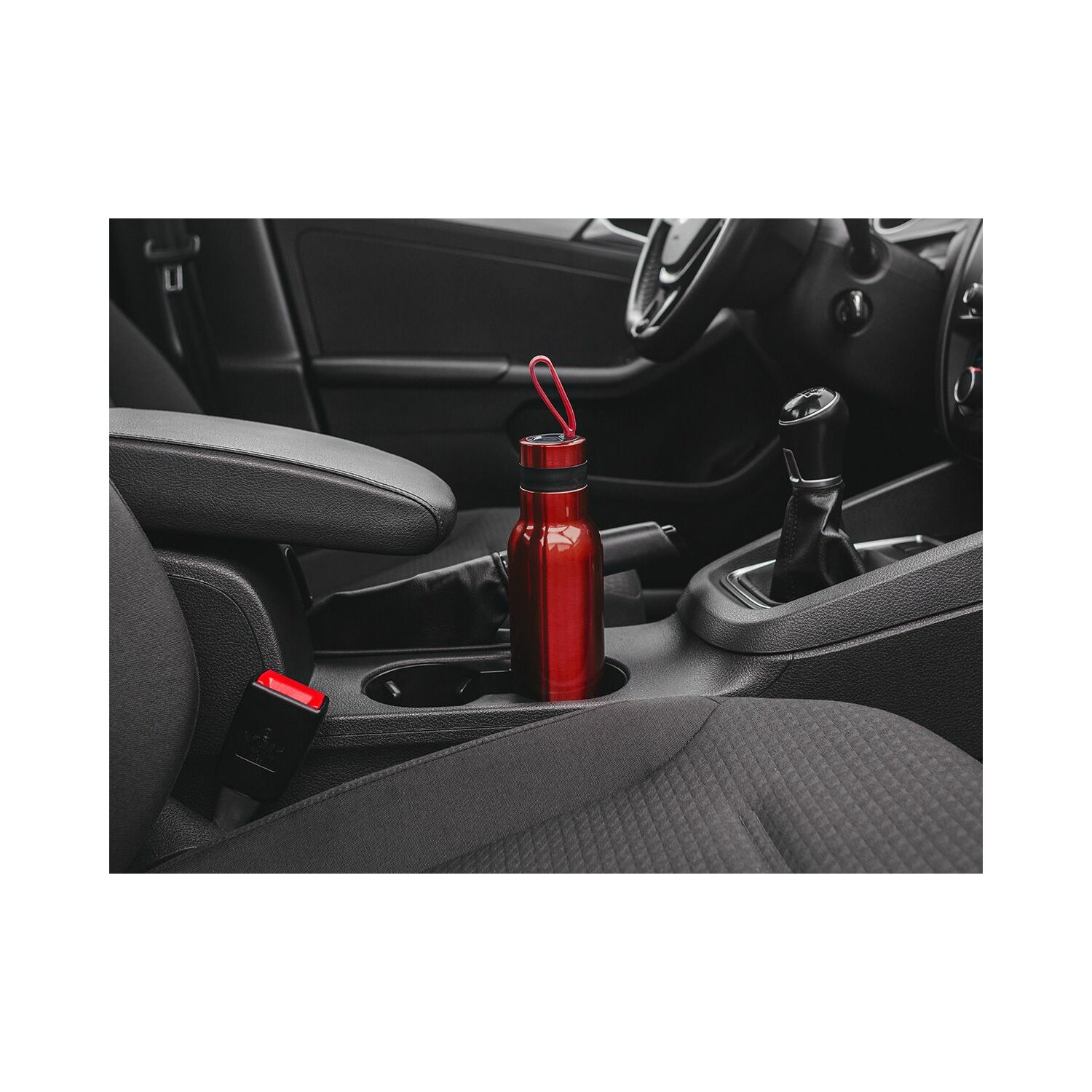 Eine rote Wasserflasche steht im Getränkehalter eines Autos. Der Innenraum ist dunkelgrau.