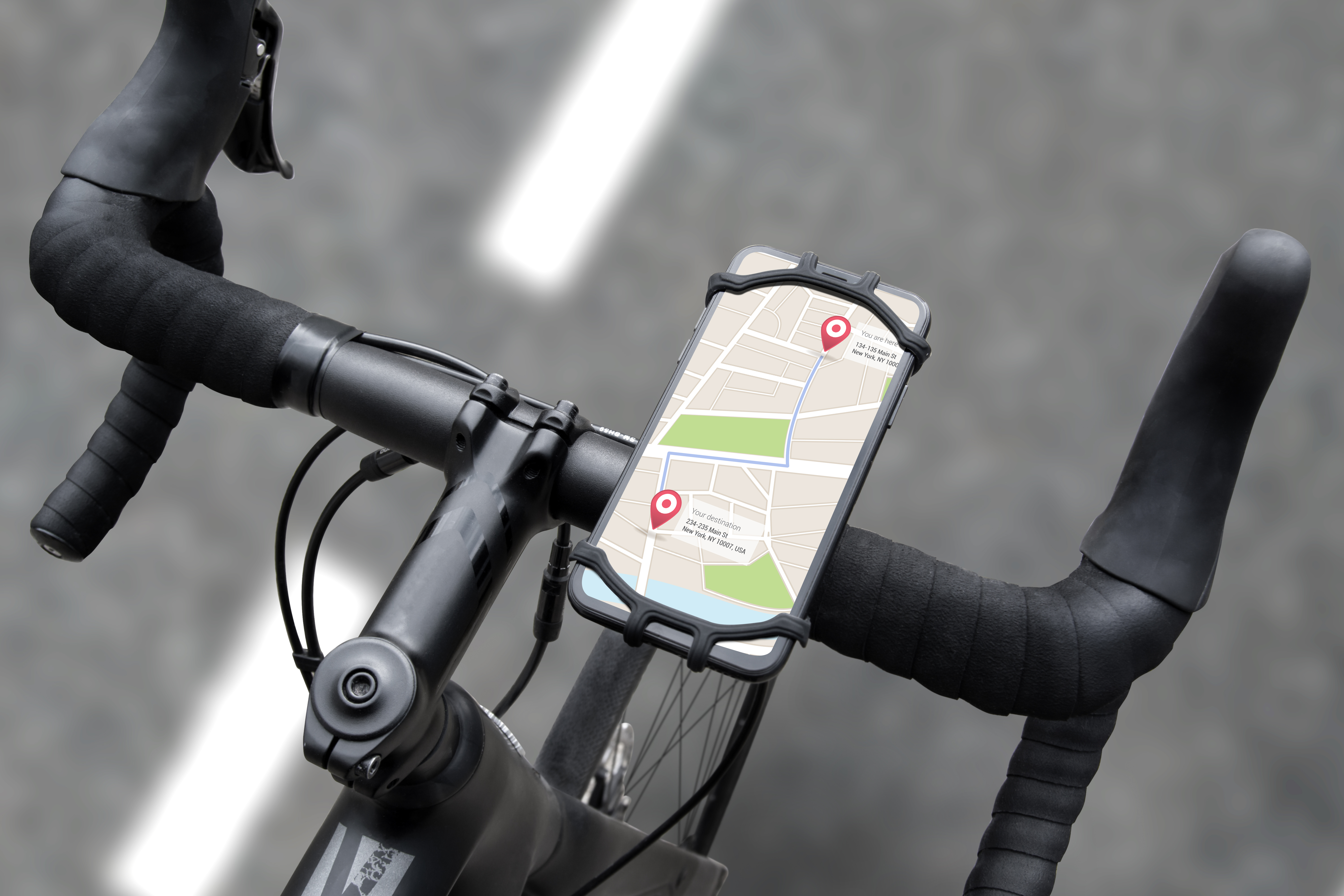 Fahrradlenker mit Telefon, das eine Karte anzeigt. Schwarze Griffe, graue Straße, Fahrradrahmen.