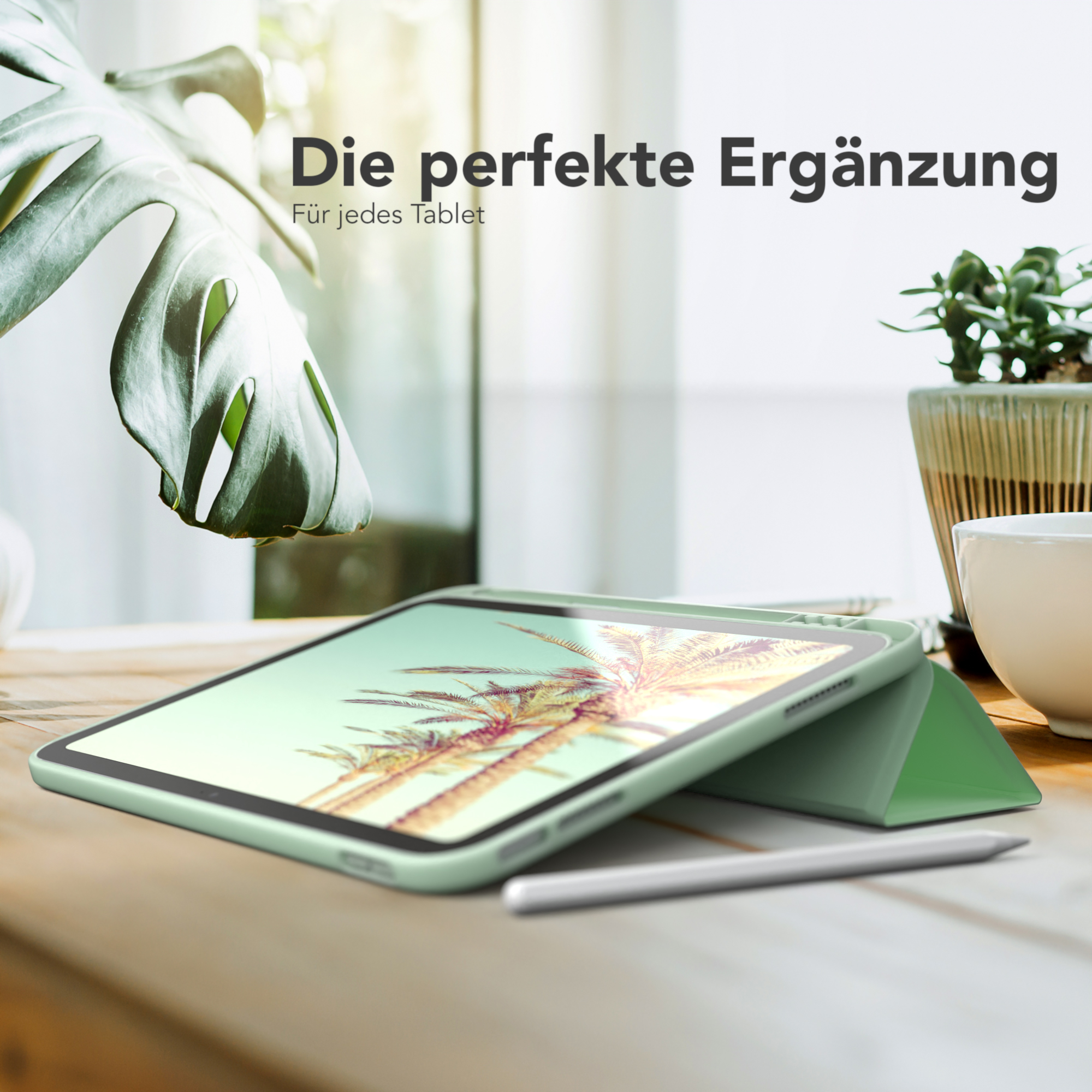 Tablet in grüner Hülle auf Holztisch, mit Stift und Pflanze im Hintergrund.