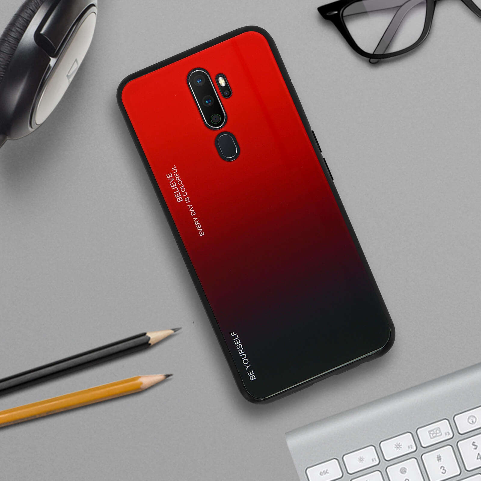 Custodia per telefono sfumata rossa e nera su una superficie grigia. Matite e tastiera visibili.