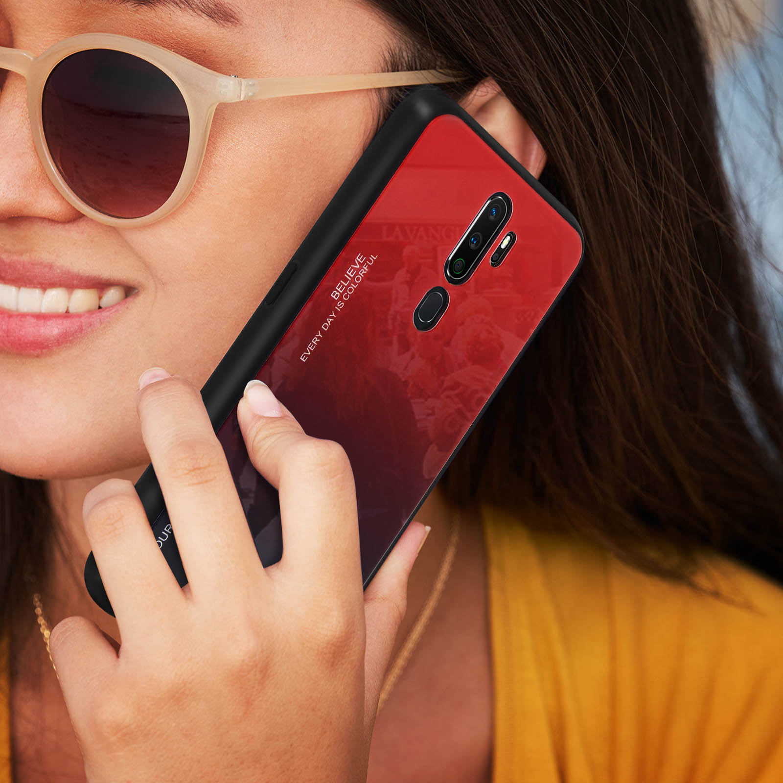 Una donna tiene un telefono sfumato rosso e nero vicino all'orecchio, indossa occhiali da sole e un top giallo.