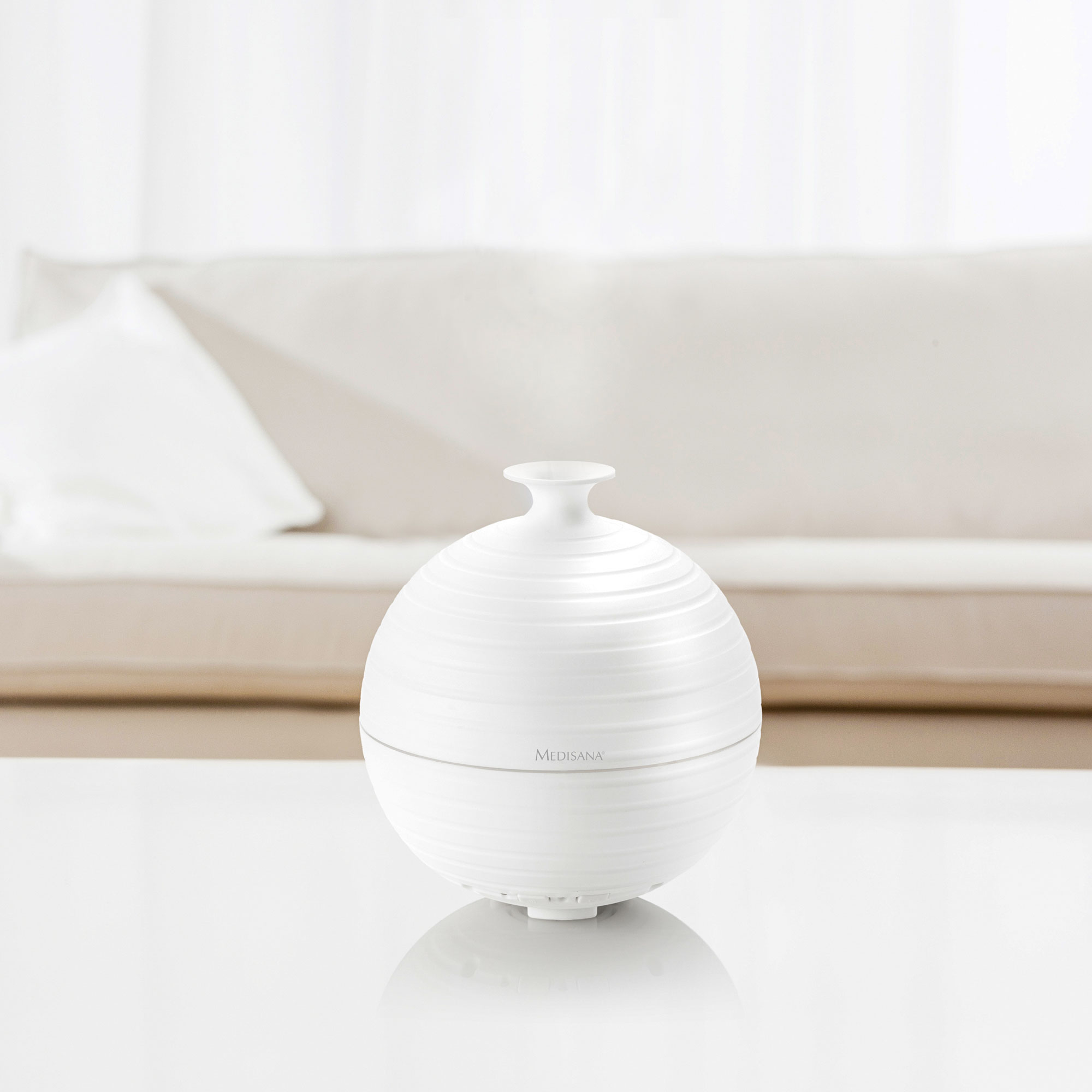Diffuseur blanc et rond sur une table blanche. Le diffuseur a un design rond et nervuré avec un petit dessus.