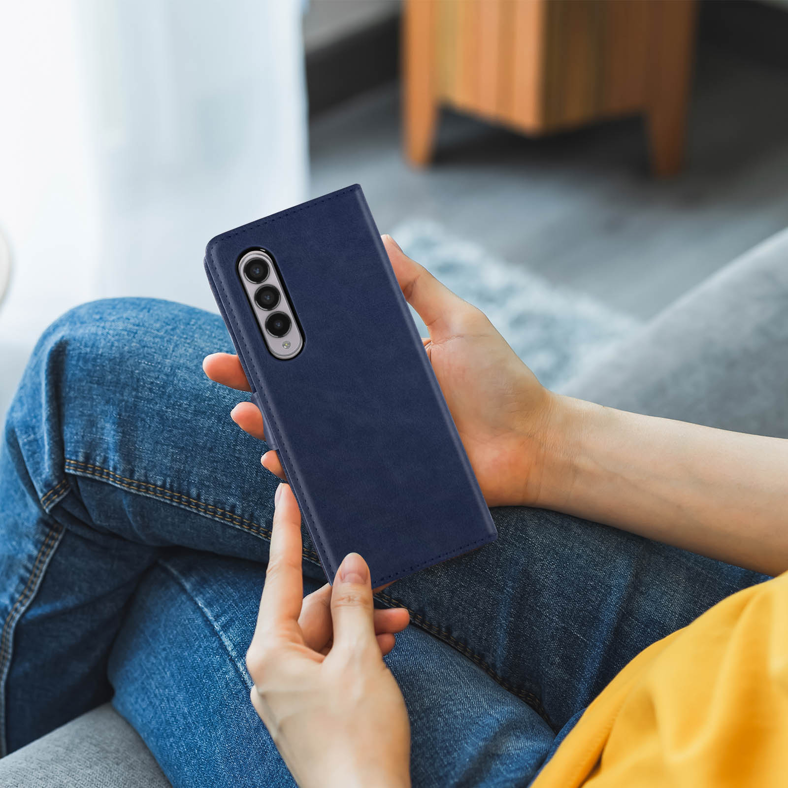 Hände halten eine blaue Handyhülle auf einer Couch.