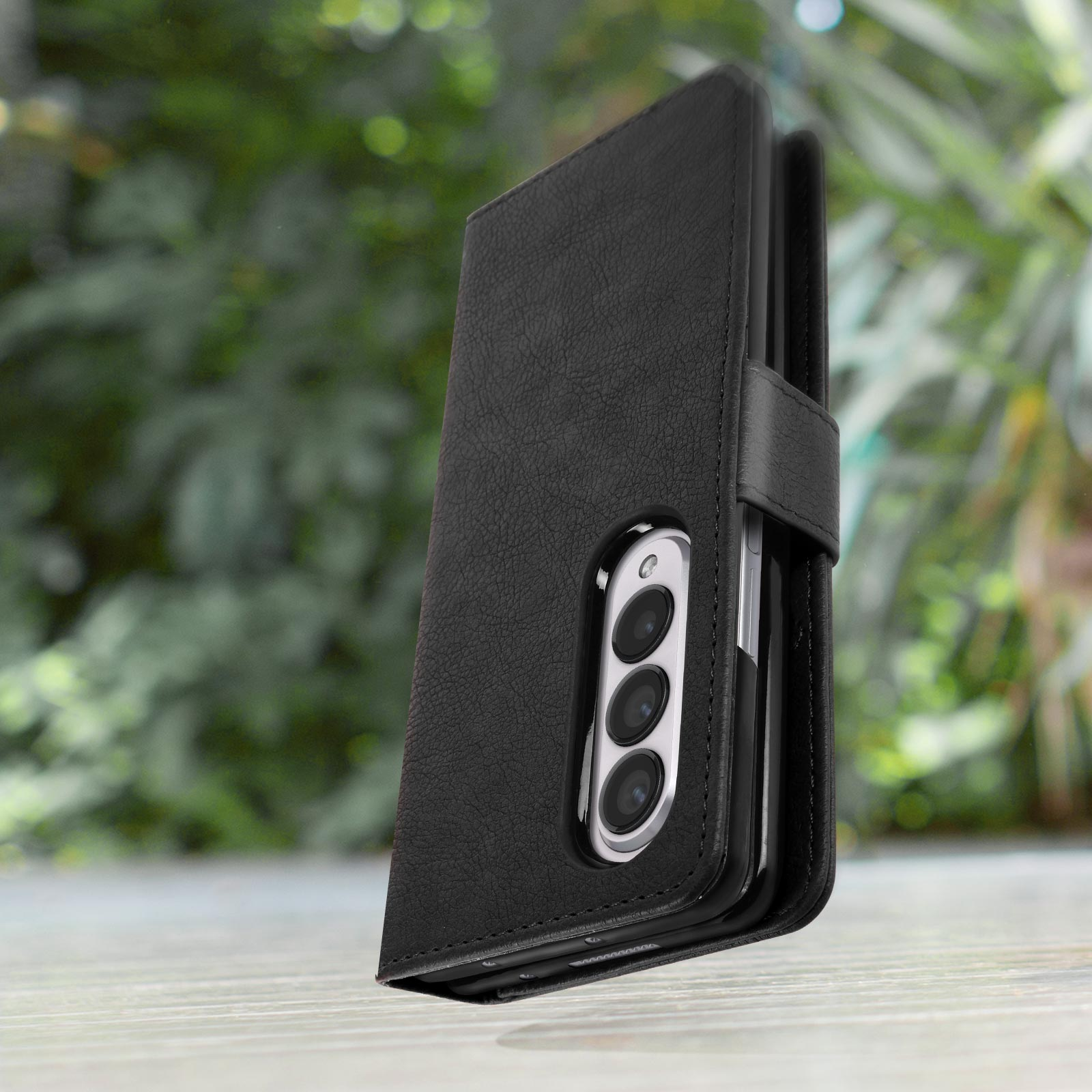 Étui de téléphone en cuir noir, téléphone inséré, fond vert. Le téléphone a trois caméras.