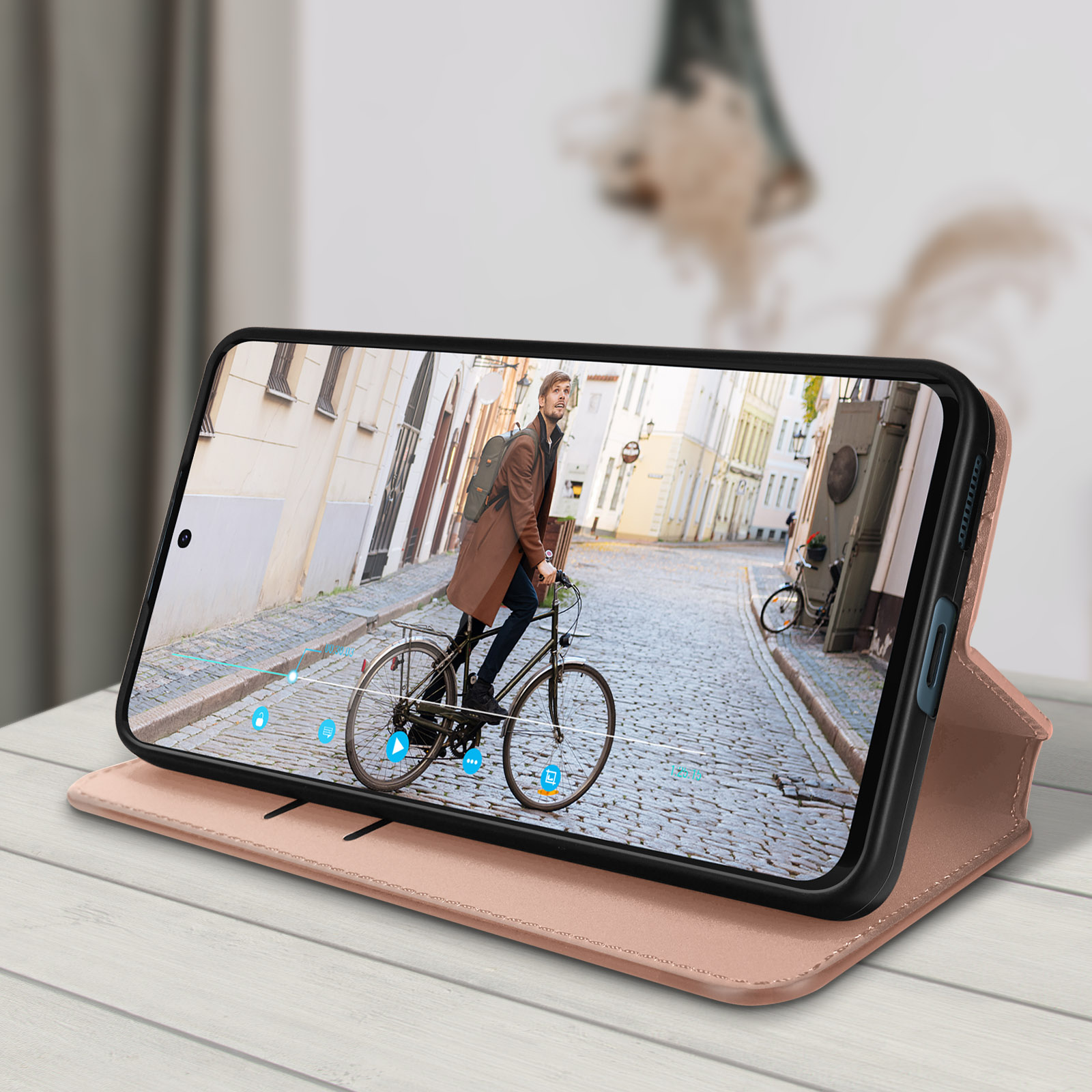 Telefono con custodia che mostra un video di una persona in bicicletta. La custodia è aperta e su una superficie di legno.