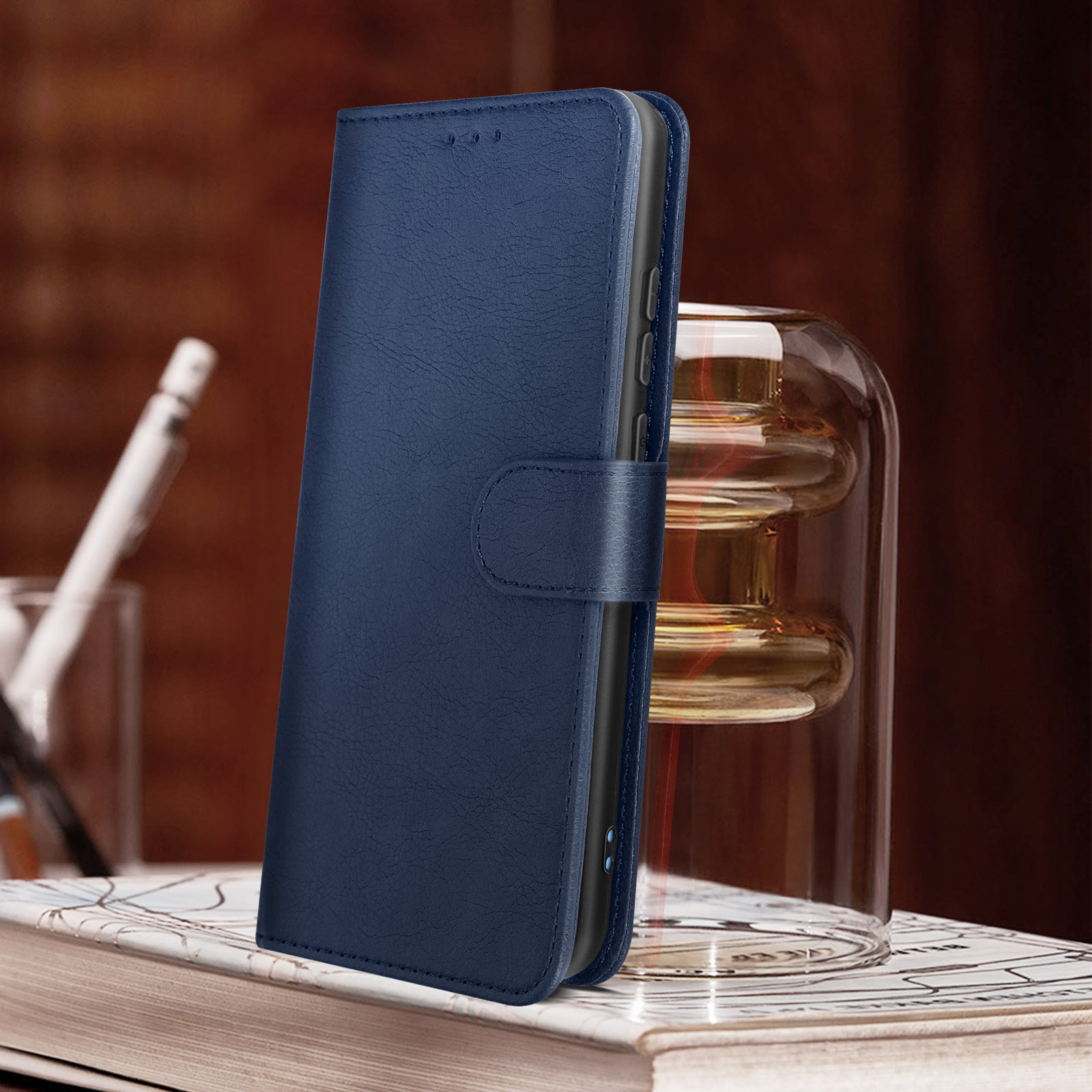 Custodia per telefono in pelle blu aperta su un libro, con una penna e un barattolo di vetro dietro.