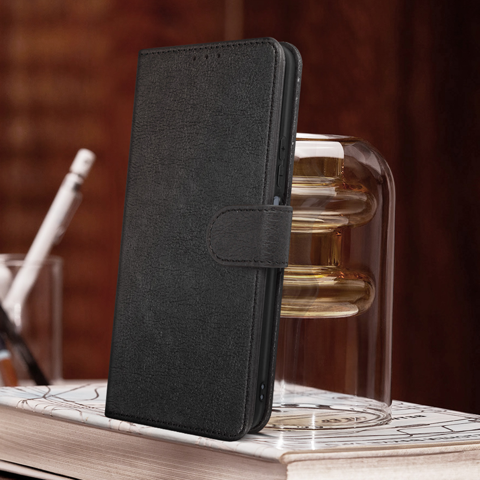 Una custodia in pelle nera appoggiata su un libro. Un vaso di vetro sullo sfondo.