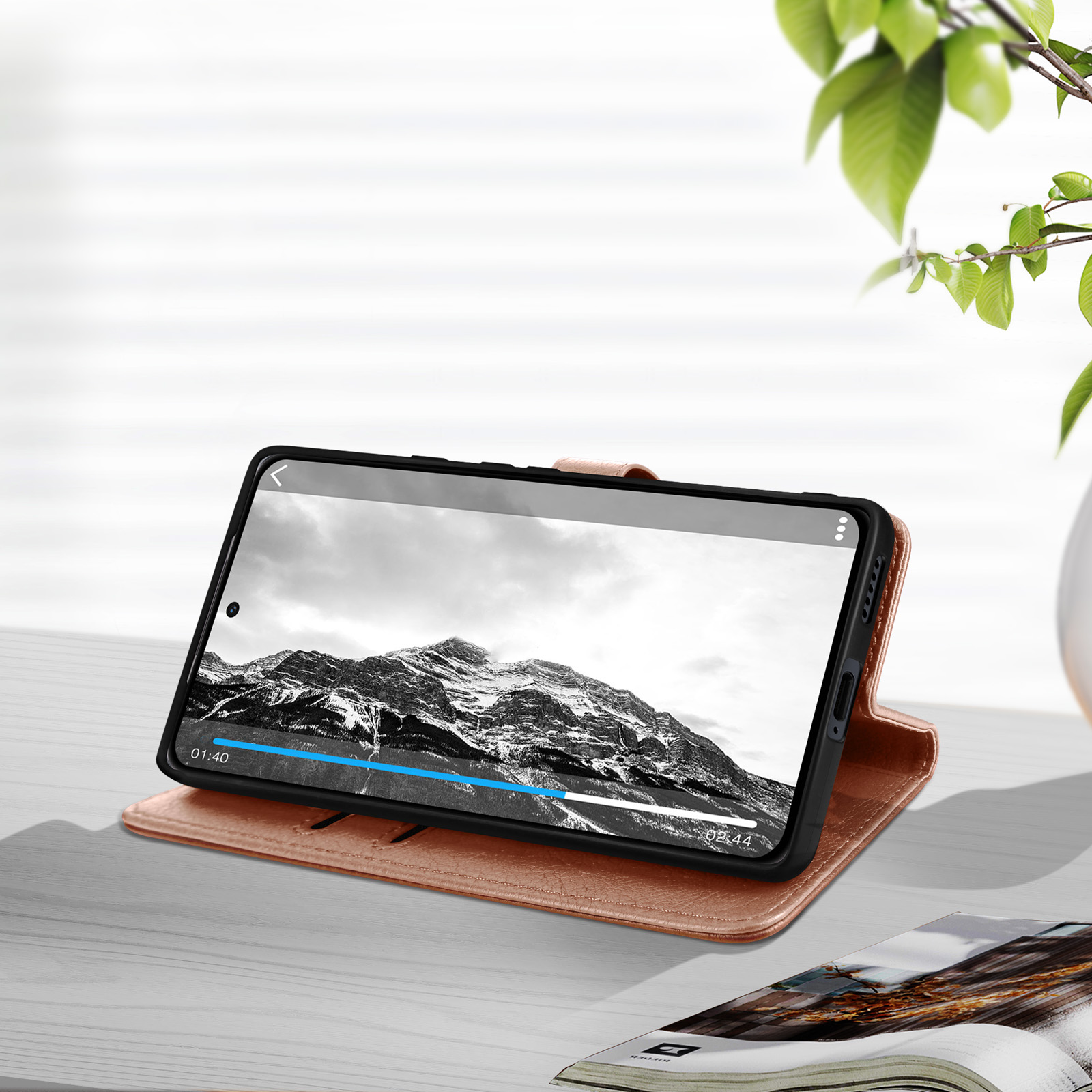 Un téléphone dans un étui marron, affichant une vidéo de montagne en noir et blanc sur une table.